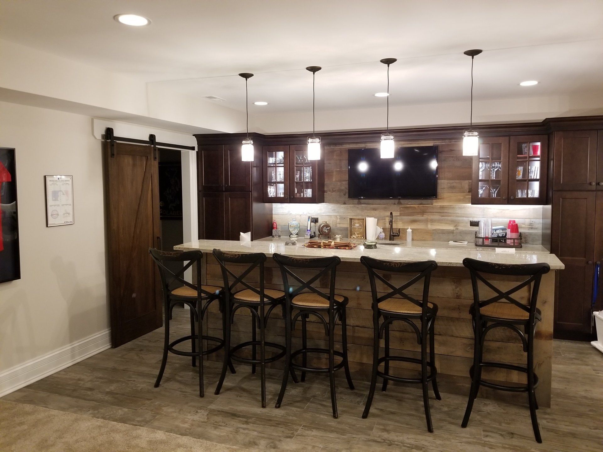Basement bar with wooden accents, bar stools, cabinets, a TV, and a sliding barn door.