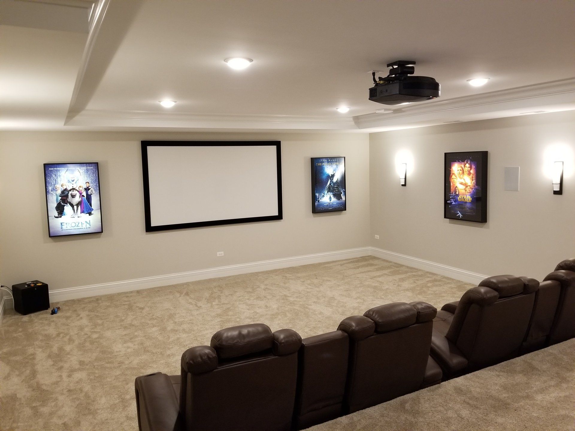 Home theater with screen, projector, recliners, movie posters, and sconces.