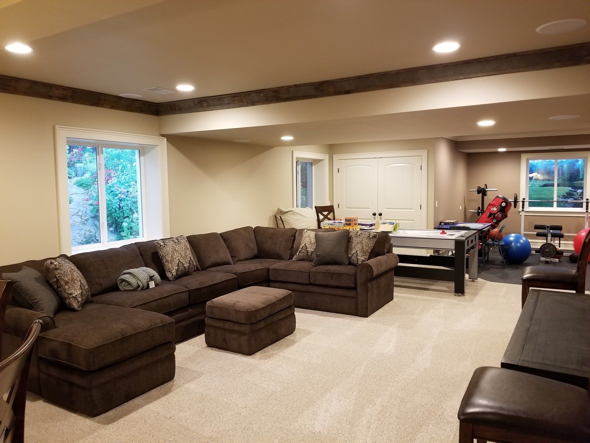 Cozy finished basement with sectional sofa, fitness equipment, and a table. Brown and tan color scheme.