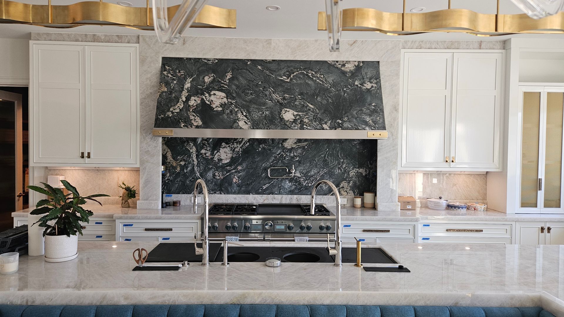 Upscale white kitchen with marble countertops and dark granite hood, gold light fixtures.
