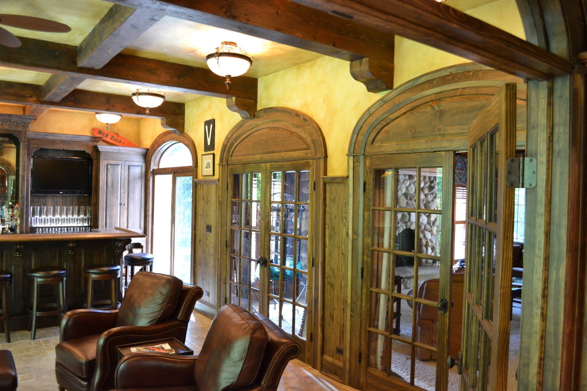 Rustic interior with wood doors, leather chairs, bar, and ceiling beams.