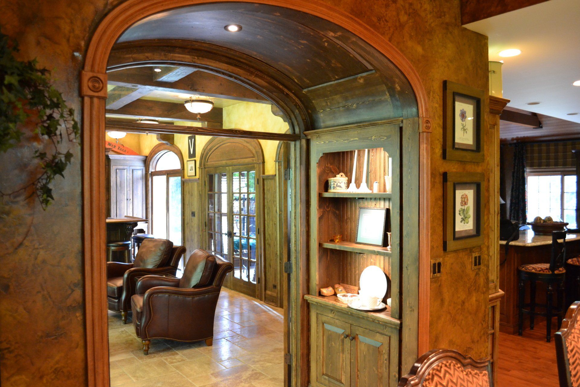 Interior view of a home with an arched doorway, bookshelves, and leather chairs; warm colors, wood accents.