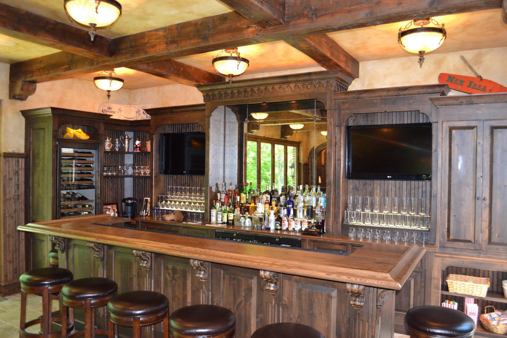 Rustic home bar with dark wood, stools, alcohol bottles, and TVs.
