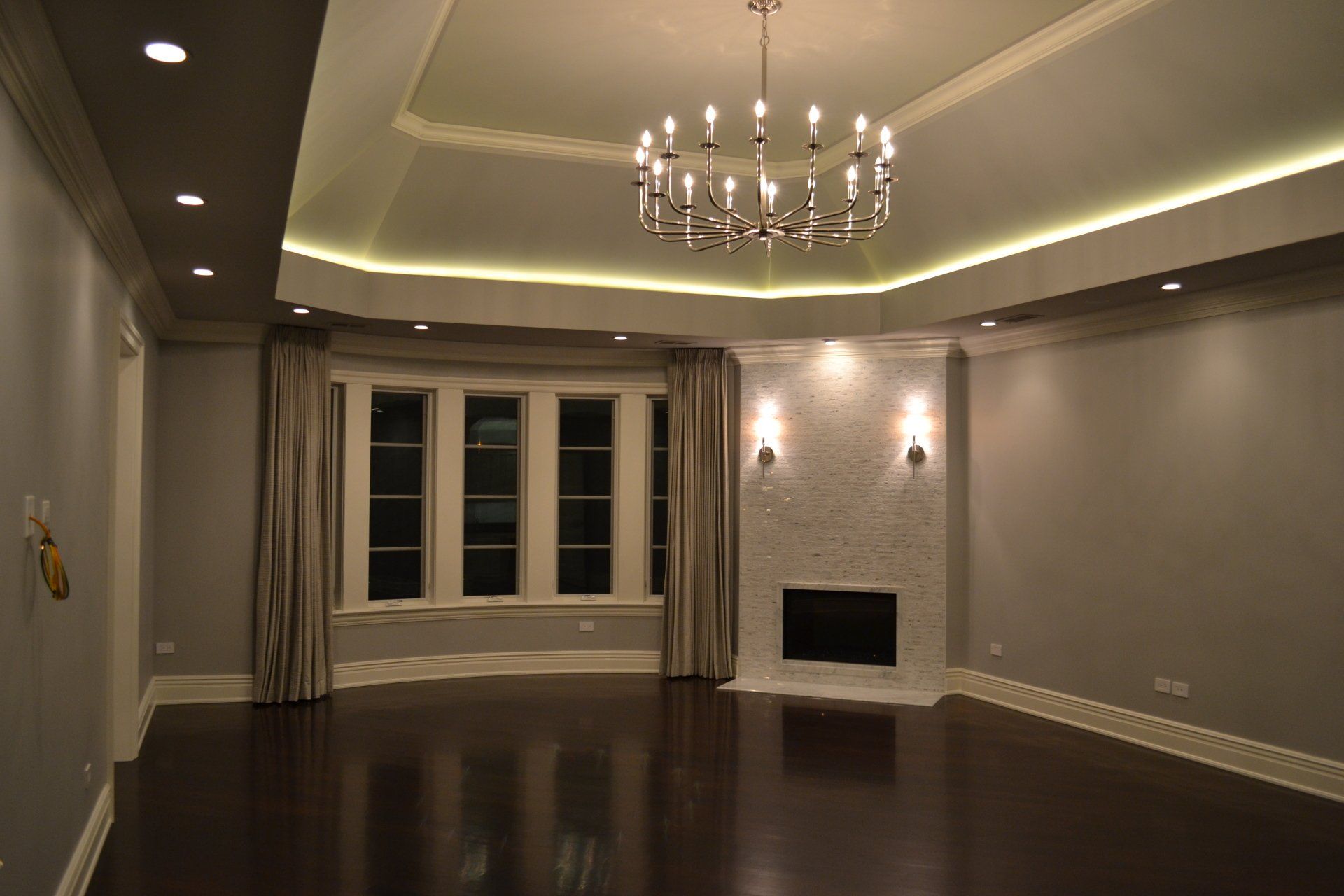 Empty living room with dark wood floors, fireplace, chandelier, and recessed lighting.