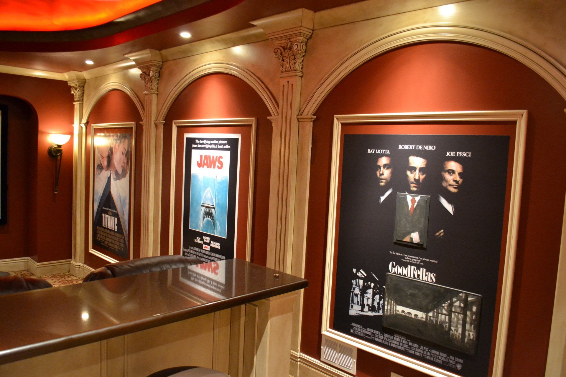 Movie posters in red-walled home theater, framed within arched alcoves, alongside a bar.
