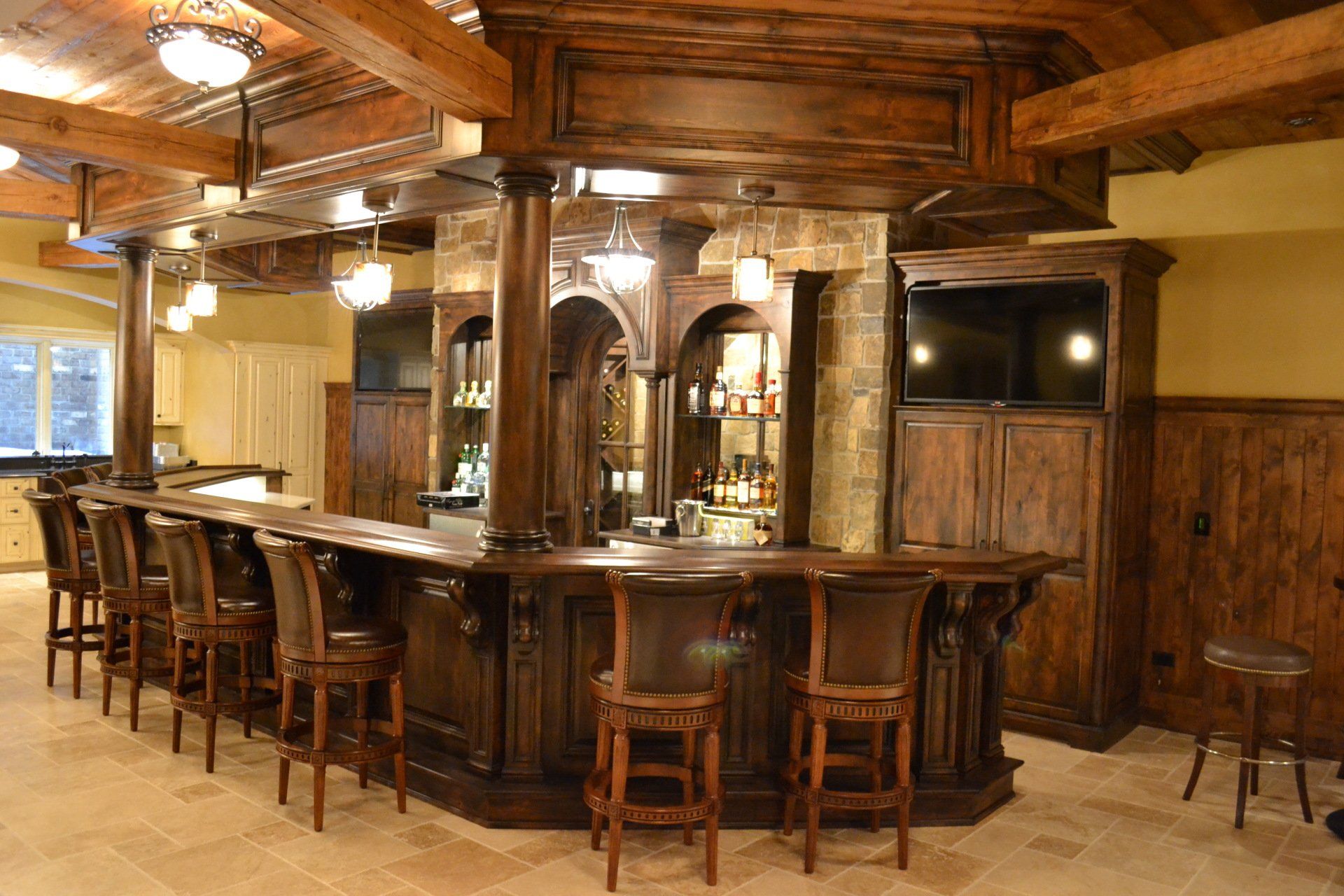 A wooden bar with barstools, liquor bottles, and a TV in a basement.