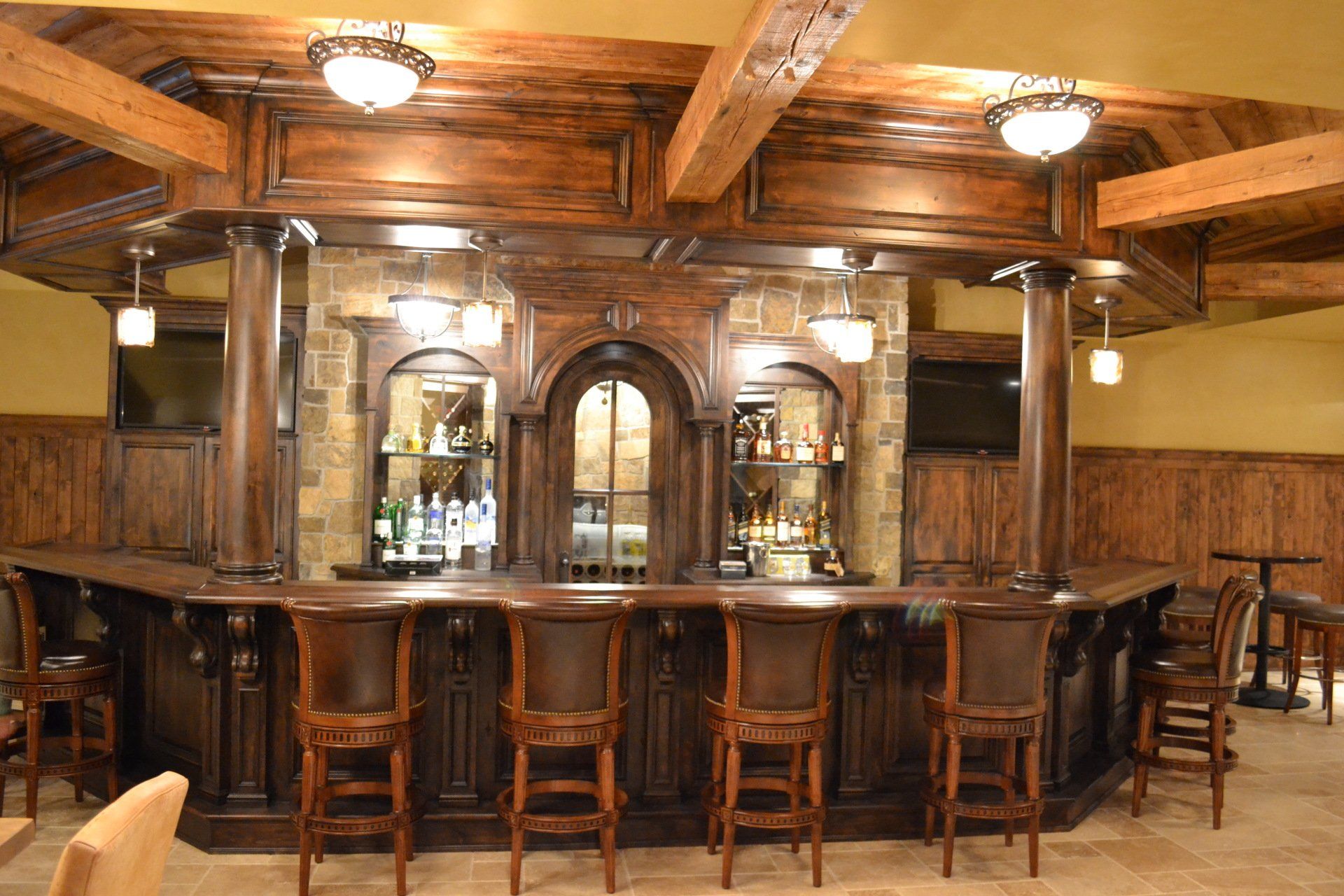 Dark wood bar with ornate detailing, bar stools, and overhead lighting.