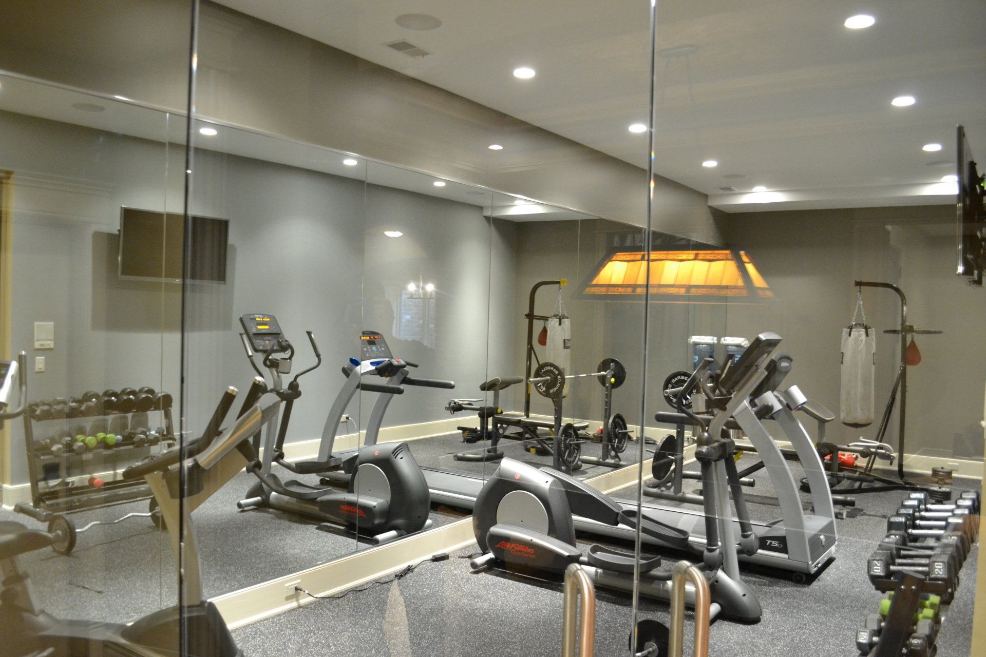 Home gym with mirrors, exercise machines, weights, and TV.