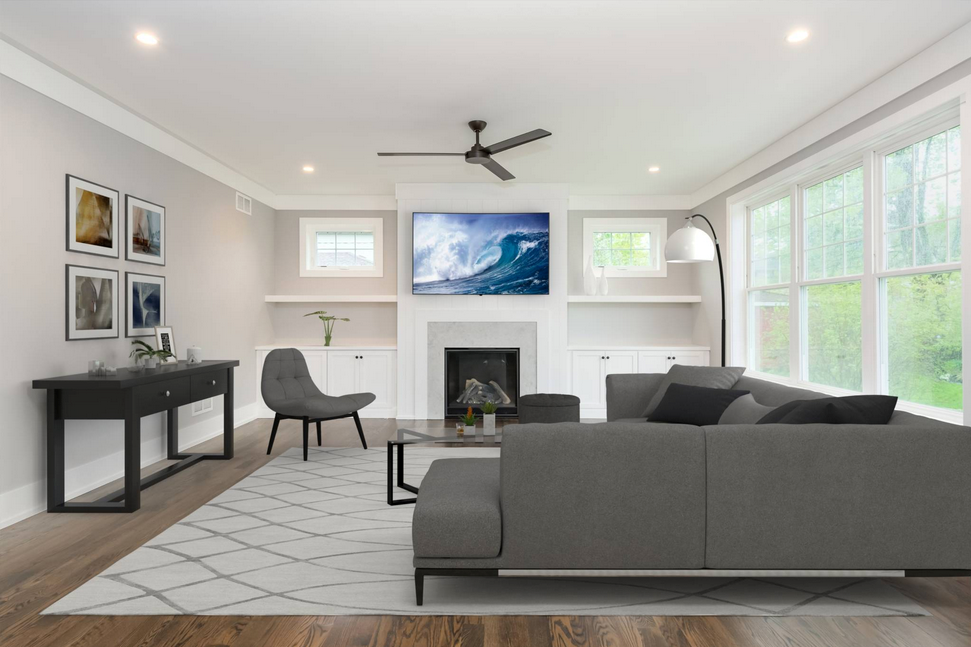 Living room with gray sofa, fireplace, built-ins, artwork, and large windows overlooking greenery.