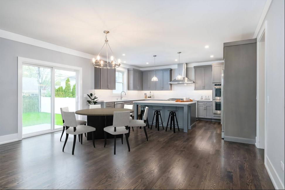 Modern kitchen with gray cabinets, island, and dining table by a sliding glass door. Dark wood floors.