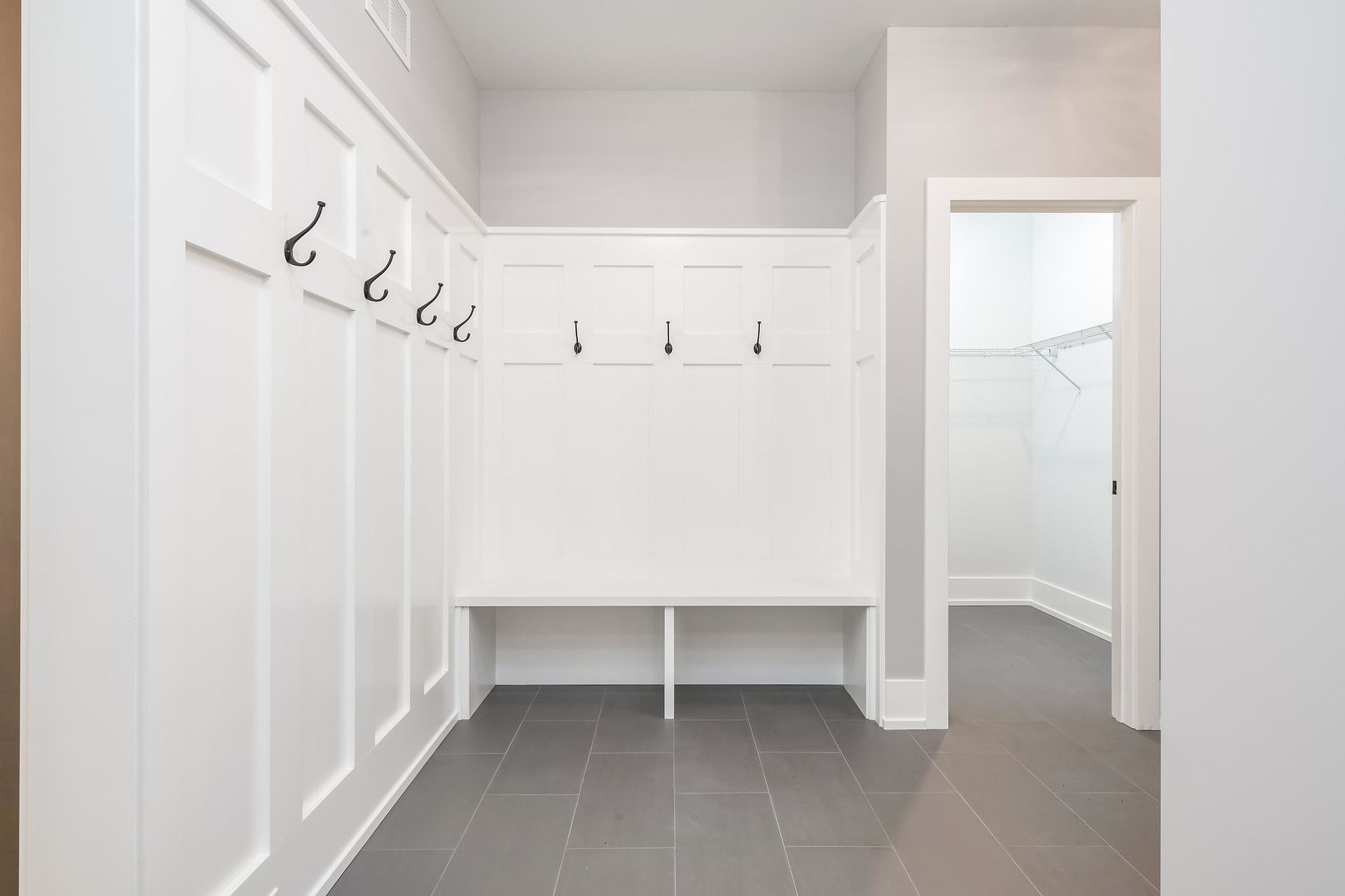 White entryway with coat hooks, bench, and tiled floor, with an open door to a closet.