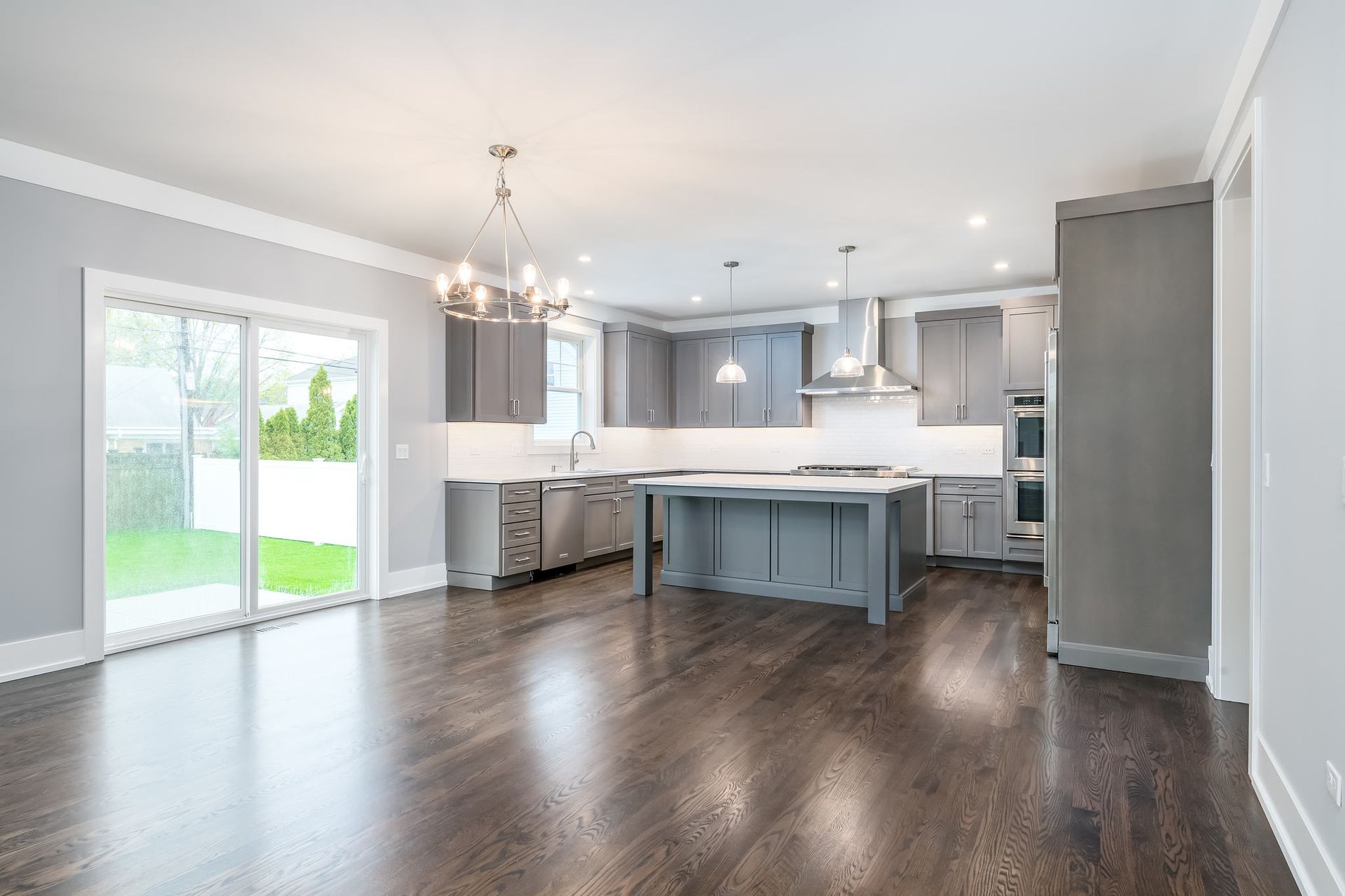 Modern kitchen with grey cabinets, dark wood floors, and a large island. Sliding glass door to the yard.