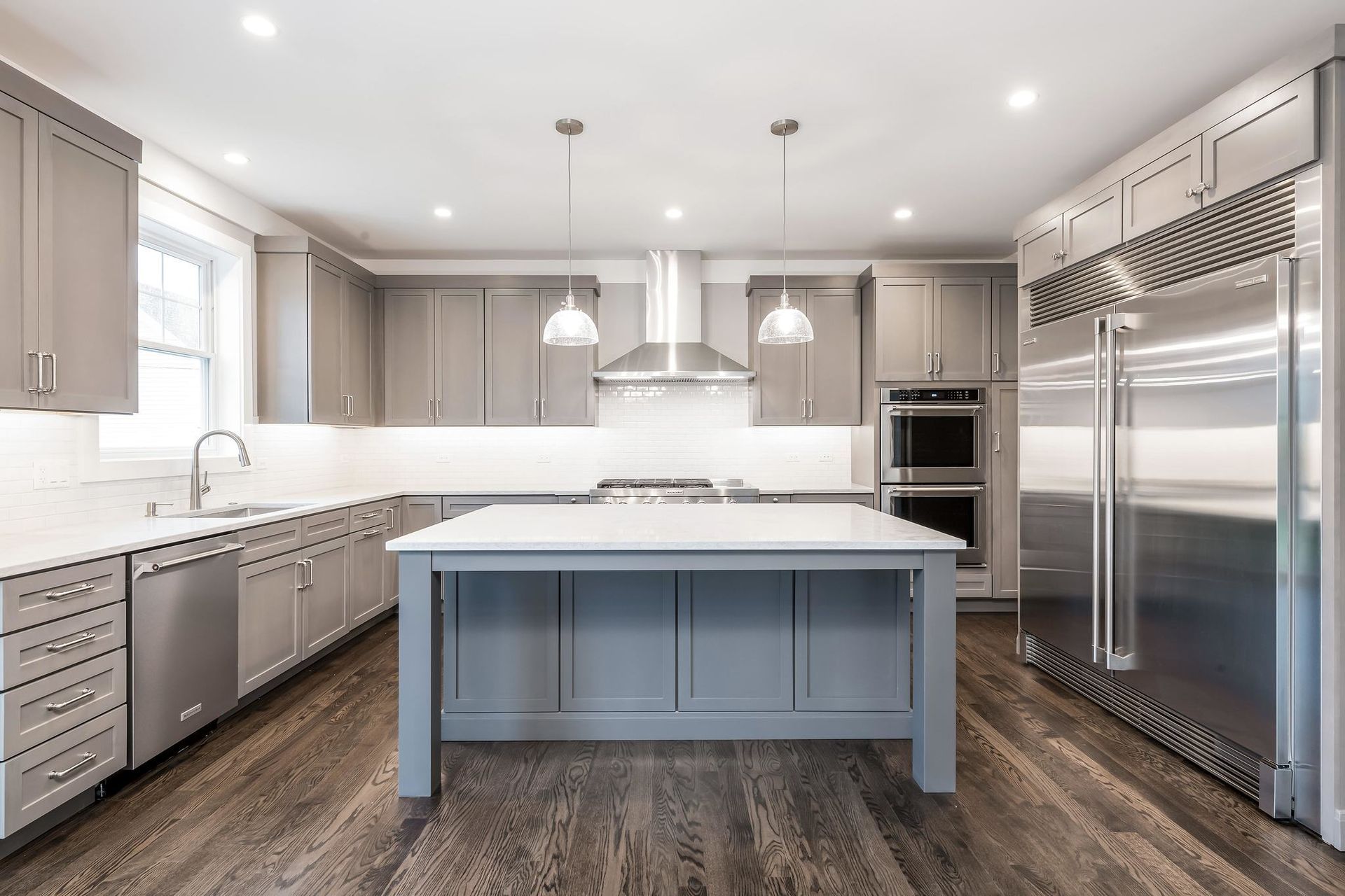Modern kitchen with gray cabinets, white countertops, stainless steel appliances, and a central island.