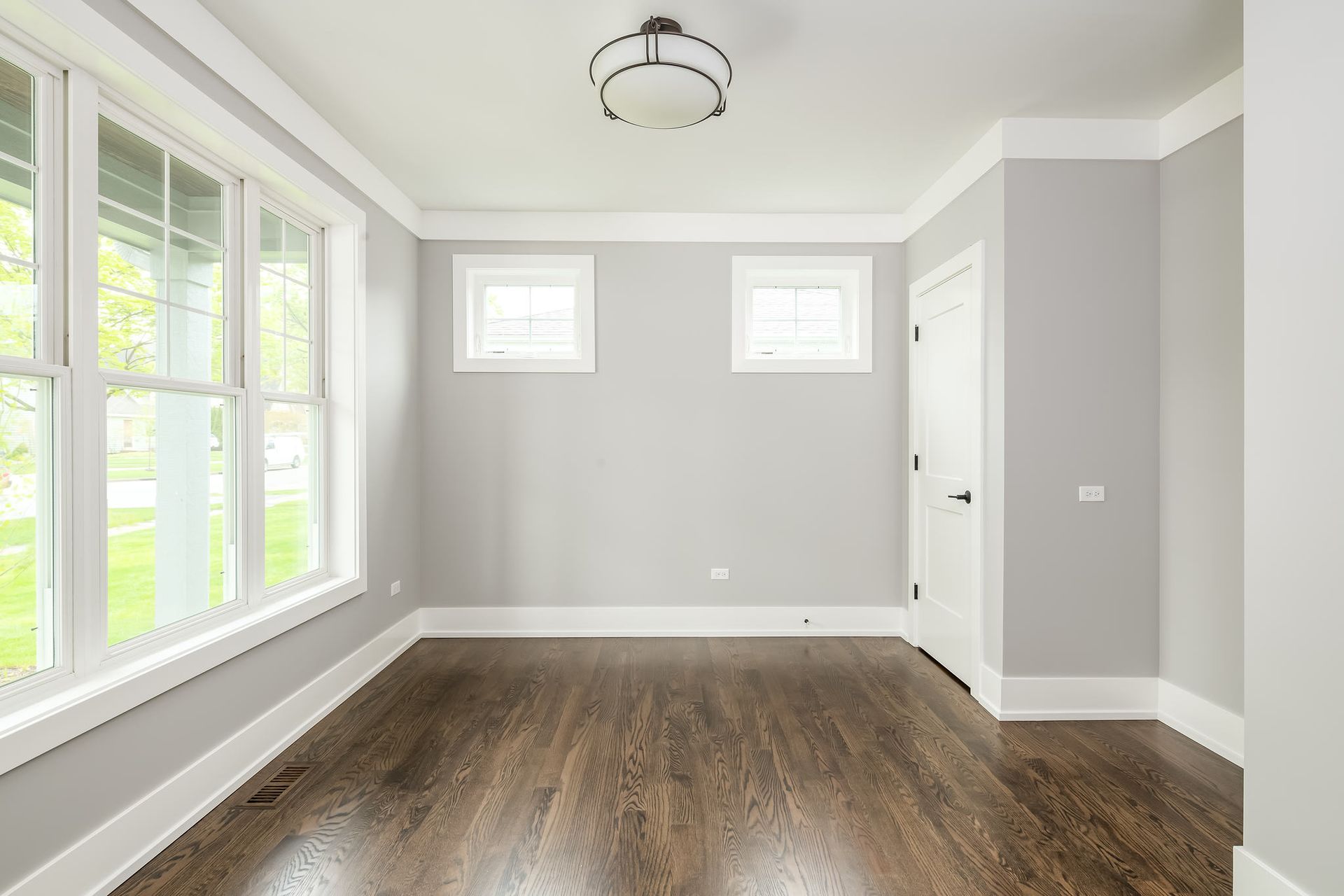Empty room with gray walls, white trim, hardwood floors, and large windows.