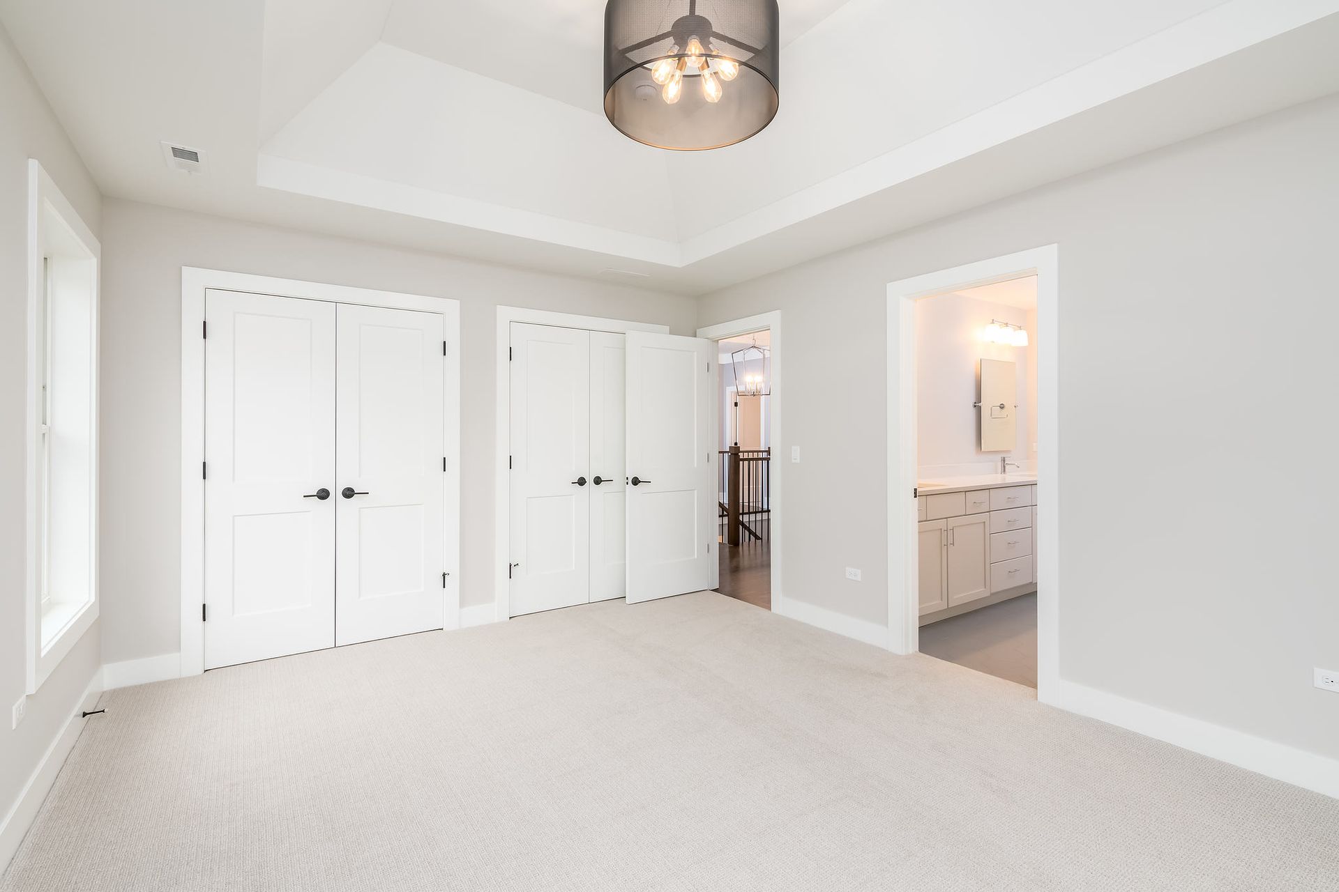 Empty bedroom with white doors, grey walls, and light carpet, leading to a bathroom.