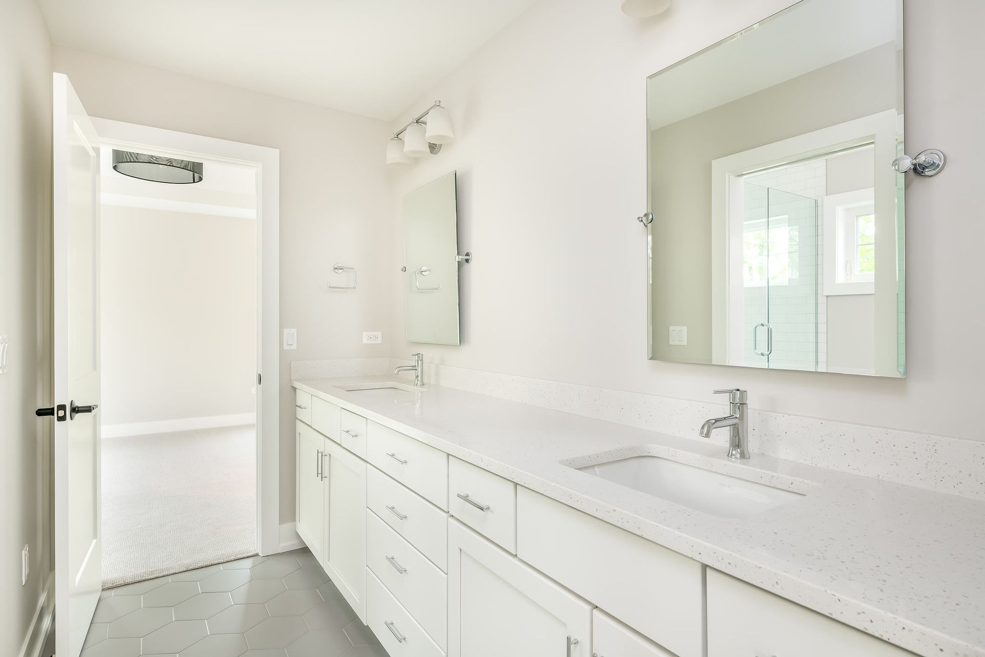 Bright white bathroom with long countertop, sinks, mirrors, and open door to a closet.