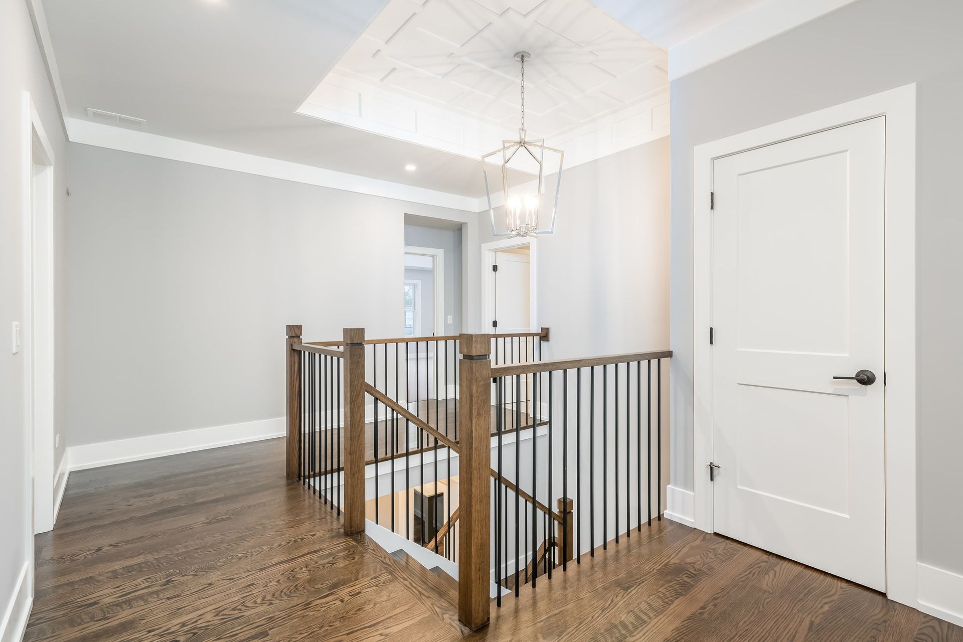 Hallway with stairs, hardwood floors, gray walls, white doors, and decorative ceiling with a hanging light fixture.