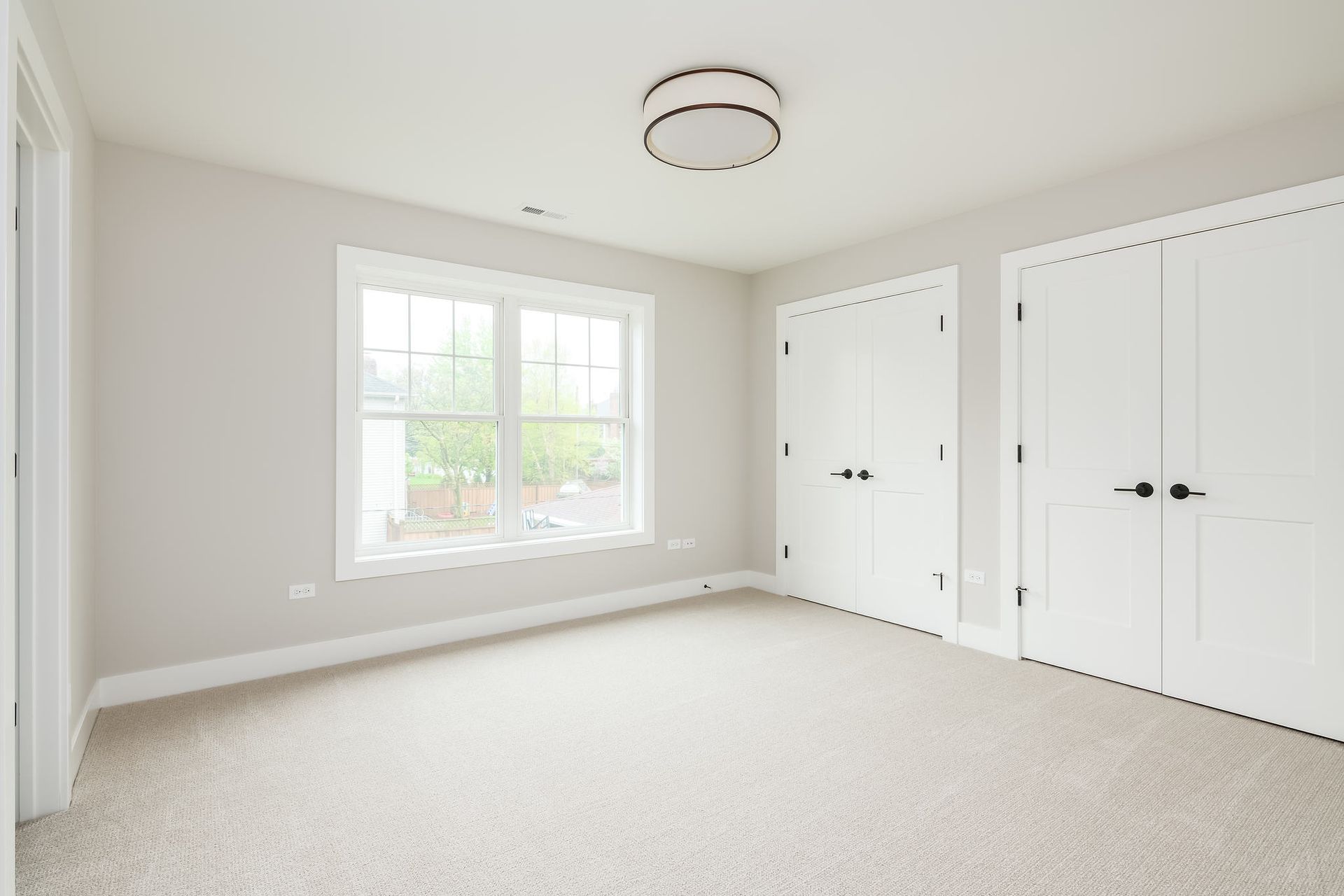 Empty bedroom with white walls, carpet, two closets, and a window.