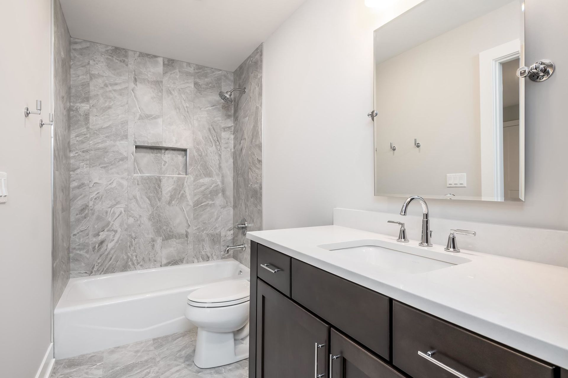 Modern bathroom with gray marble tile, white vanity, and a dark wood cabinet.