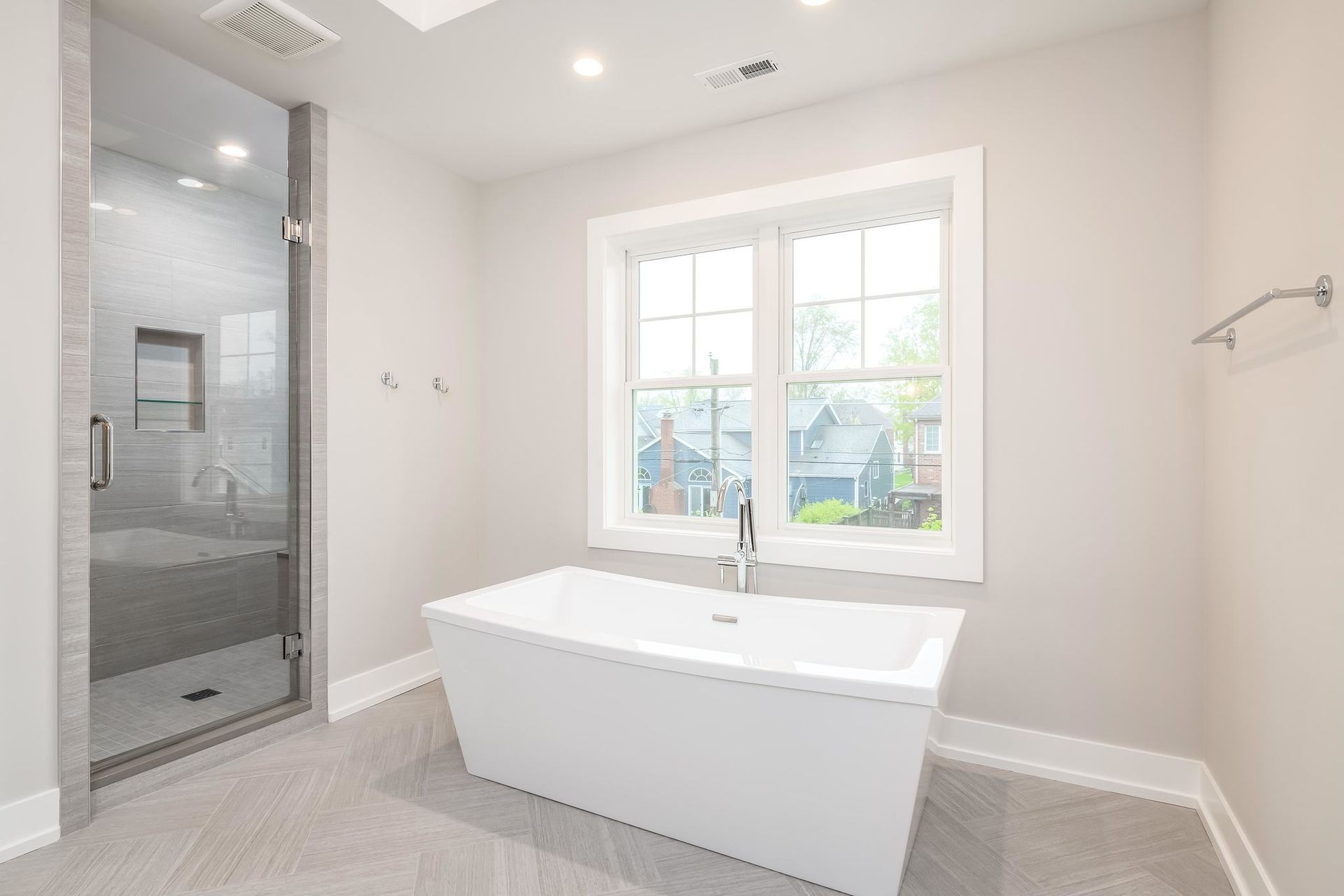 Modern bathroom with a white tub, glass shower, and window, all with light-colored walls and flooring.