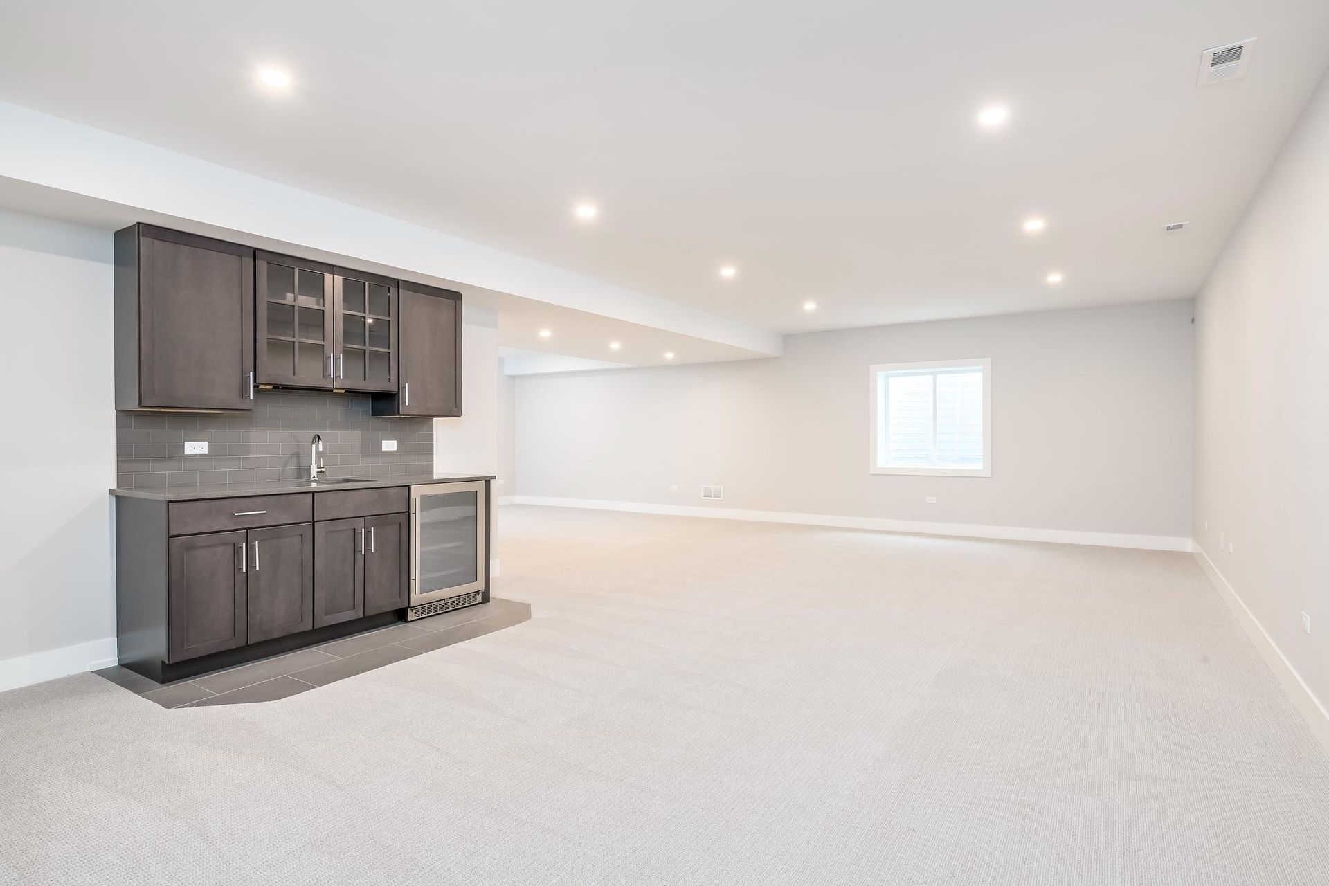 Finished basement with a dark grey bar, light carpet, and recessed lighting.