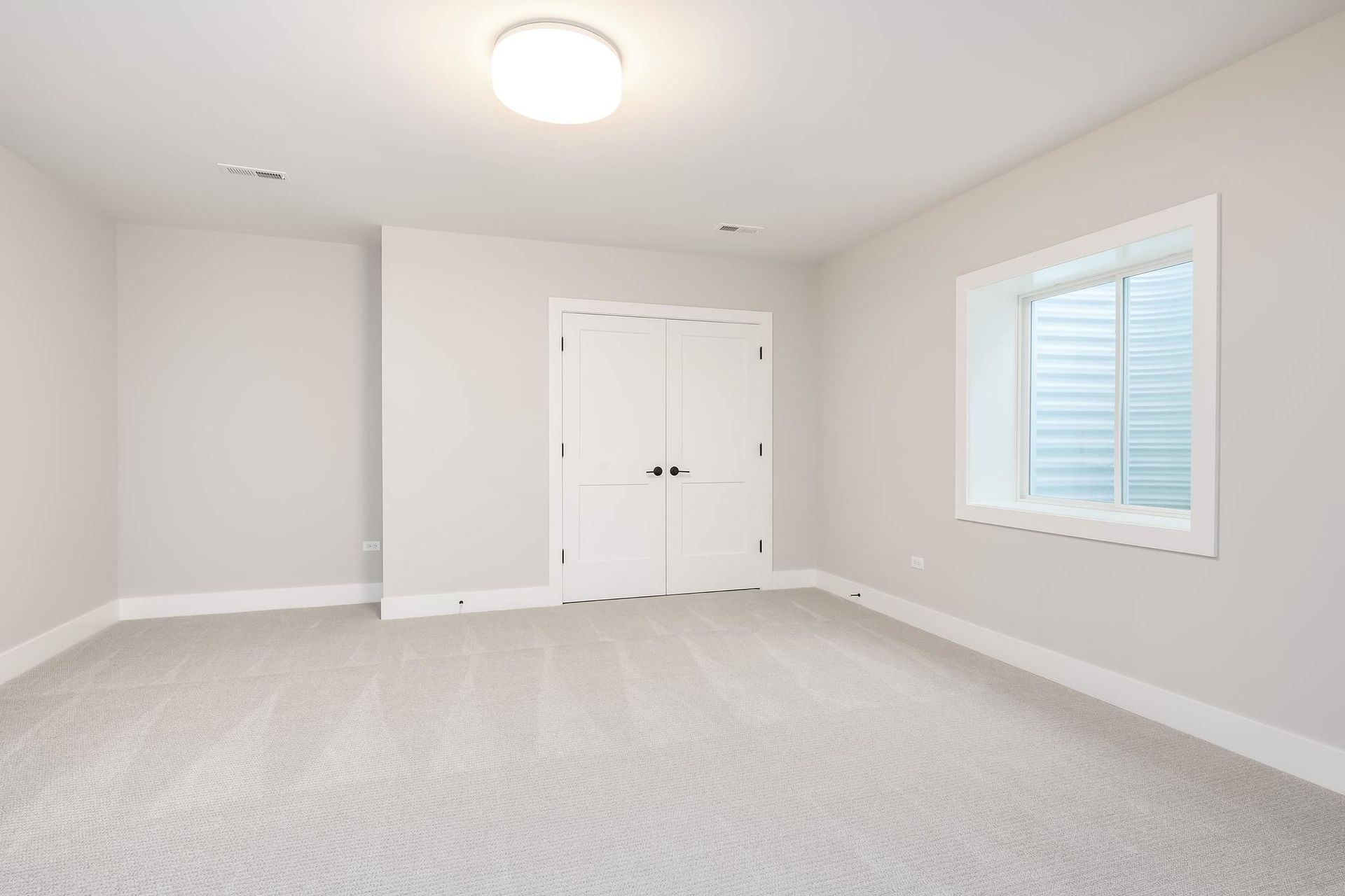 Empty room with light gray carpet, white walls, closed doors, and small window.