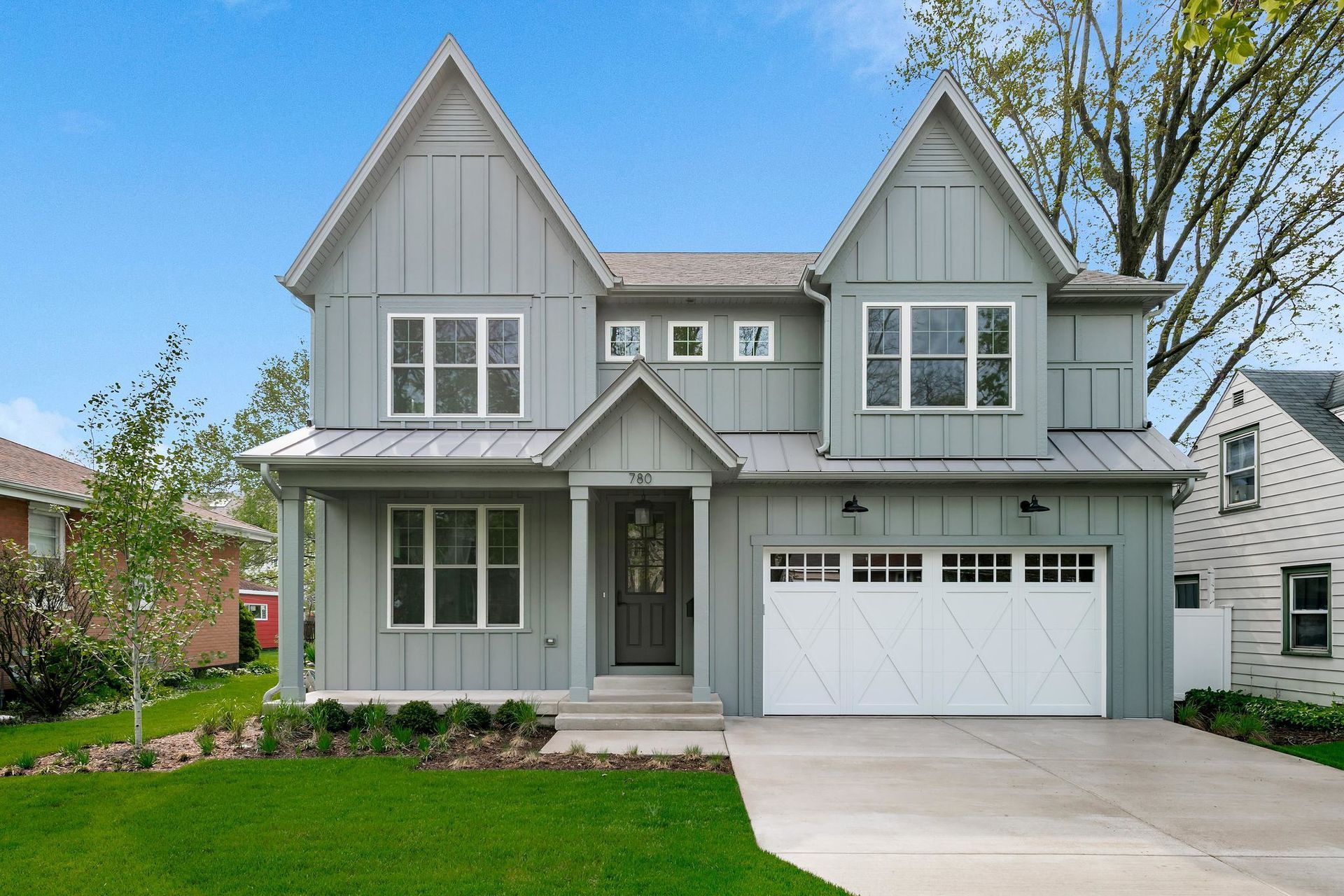 Gray two-story house with white garage door, green lawn, and blue sky.