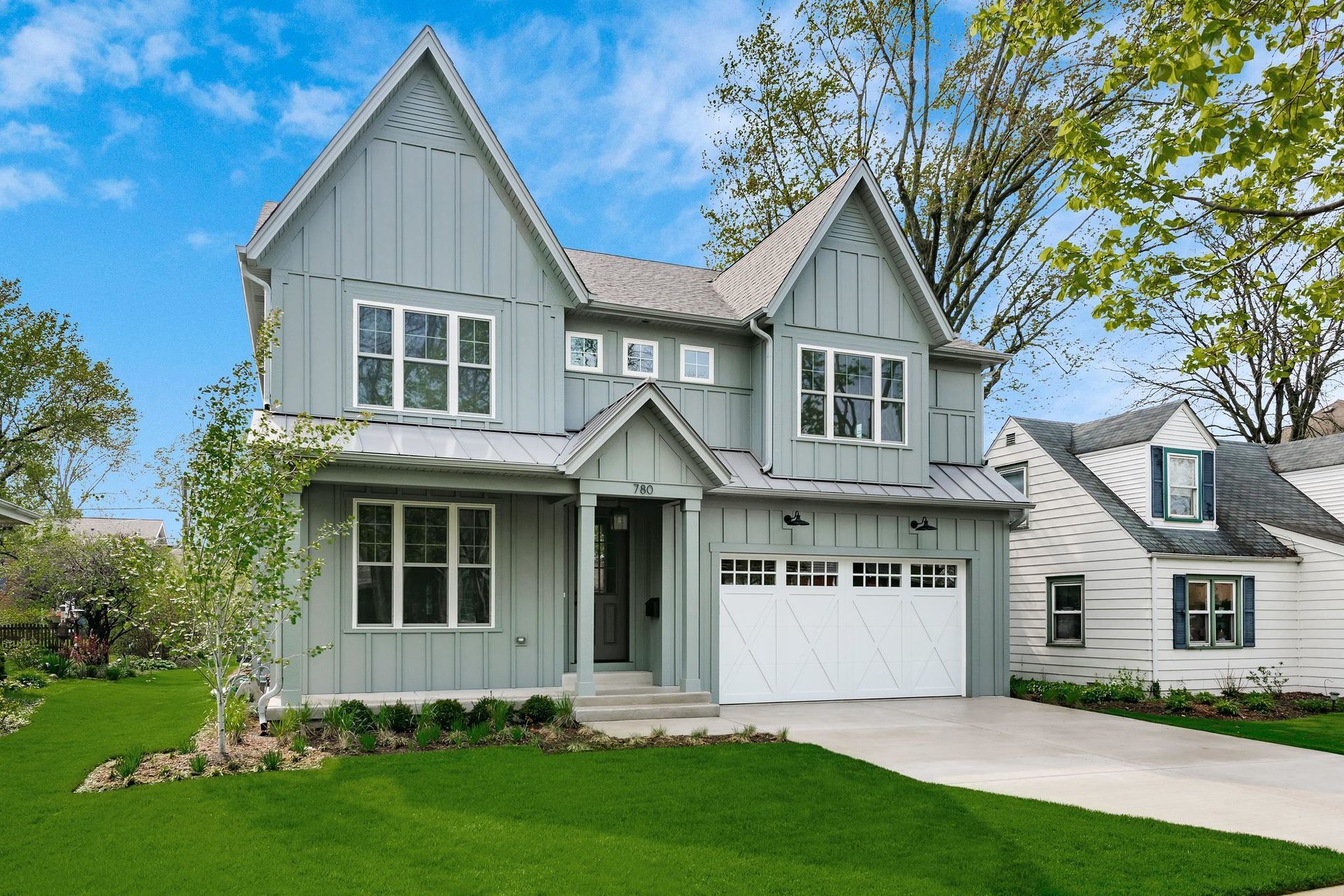 Gray two-story house with white garage door, green lawn, and a sunny blue sky.