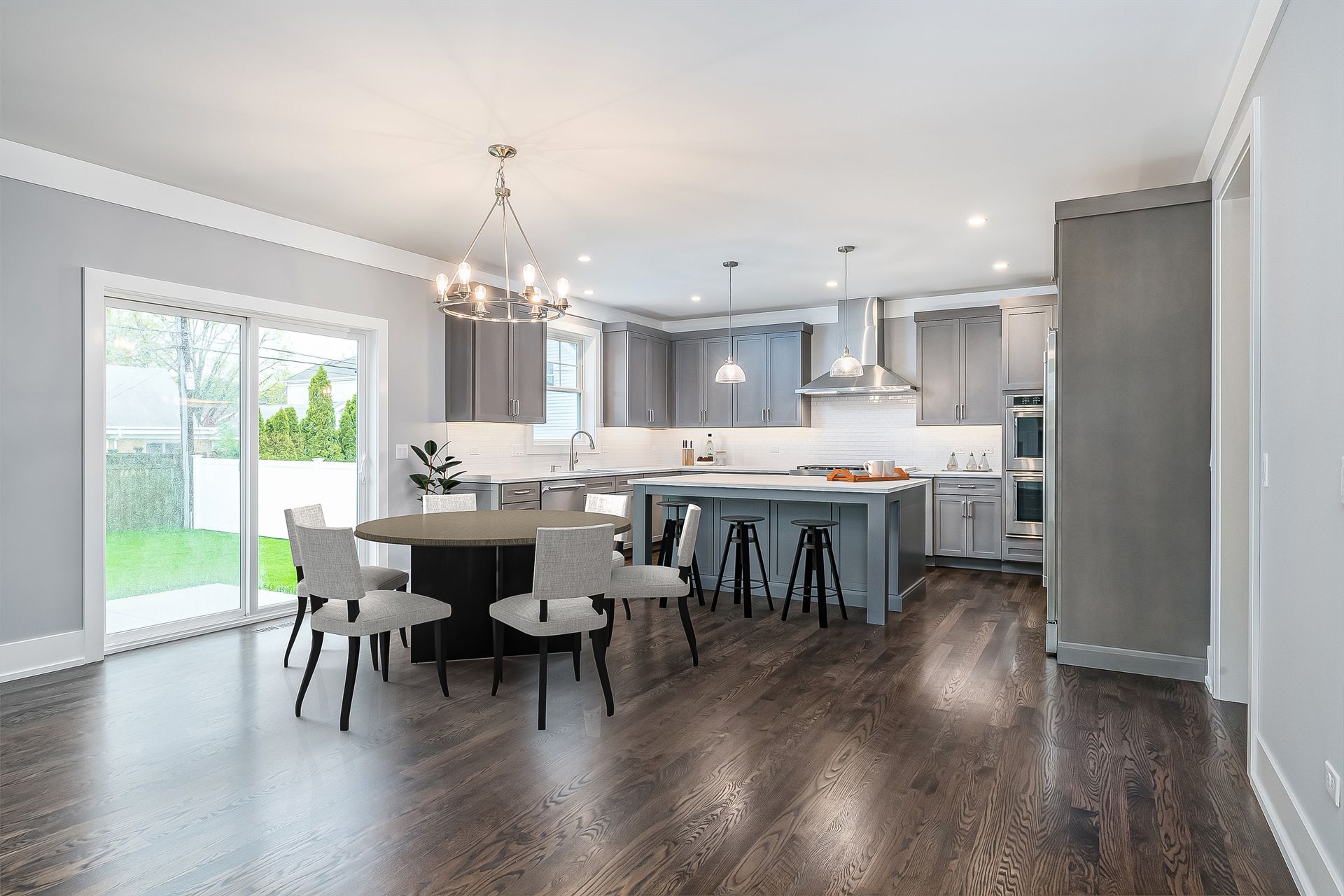 Modern kitchen and dining area with gray cabinets, a central island, and a dark wood floor.