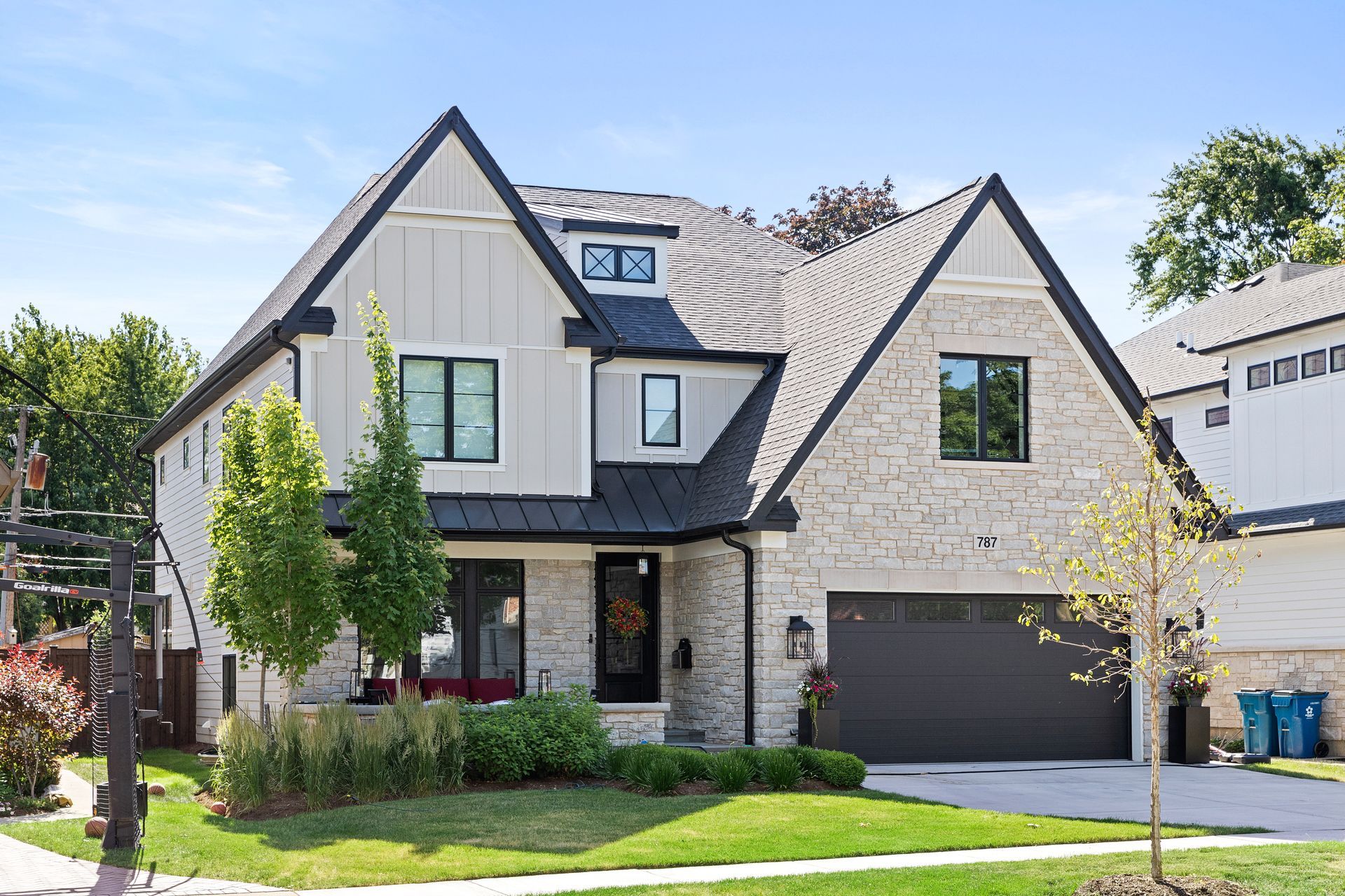 Two-story modern house with stone and light siding, black roof and trim, garage, and small front yard.