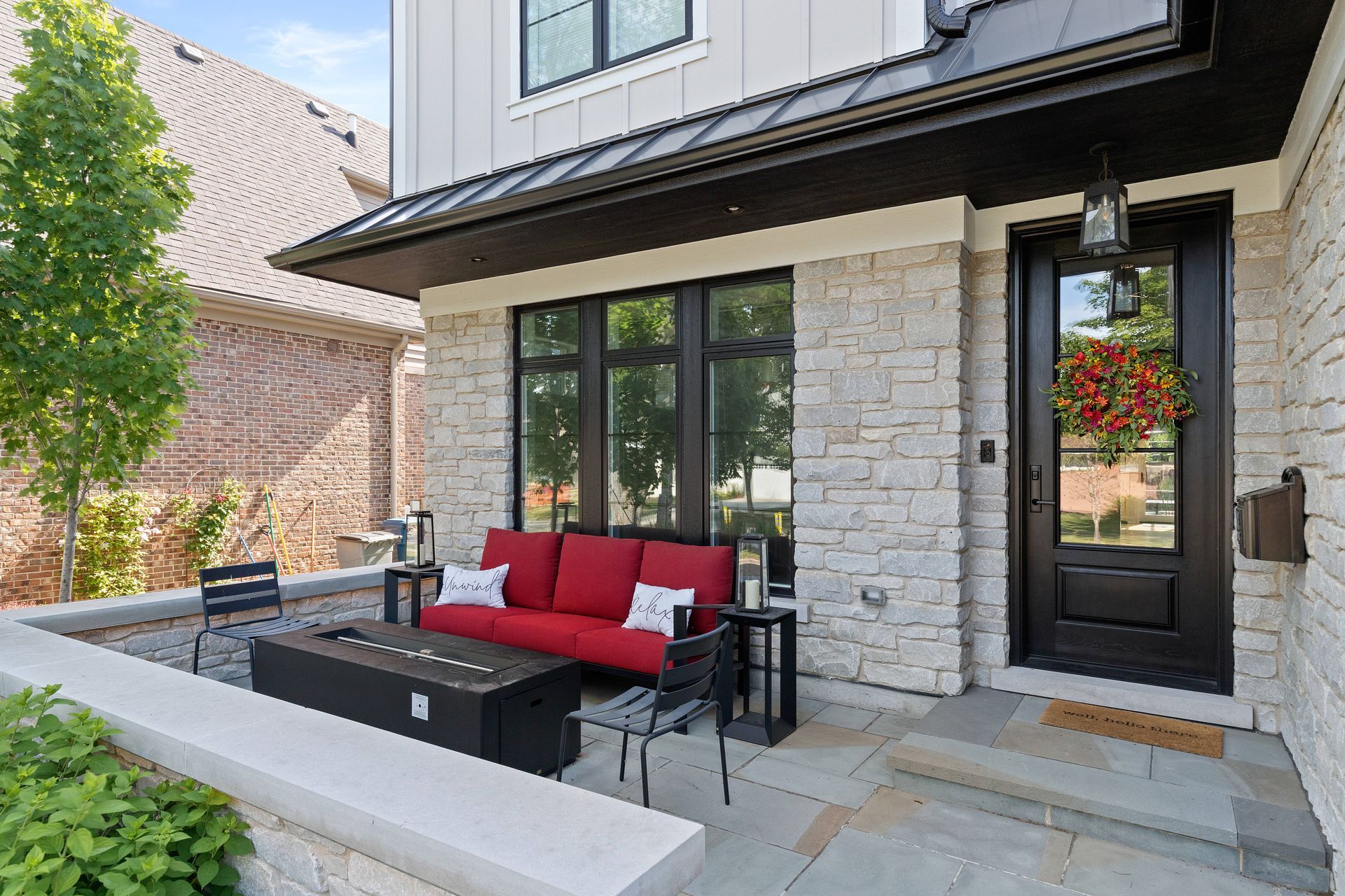 Front porch with red couch, fireplace, black door, and stone facade.