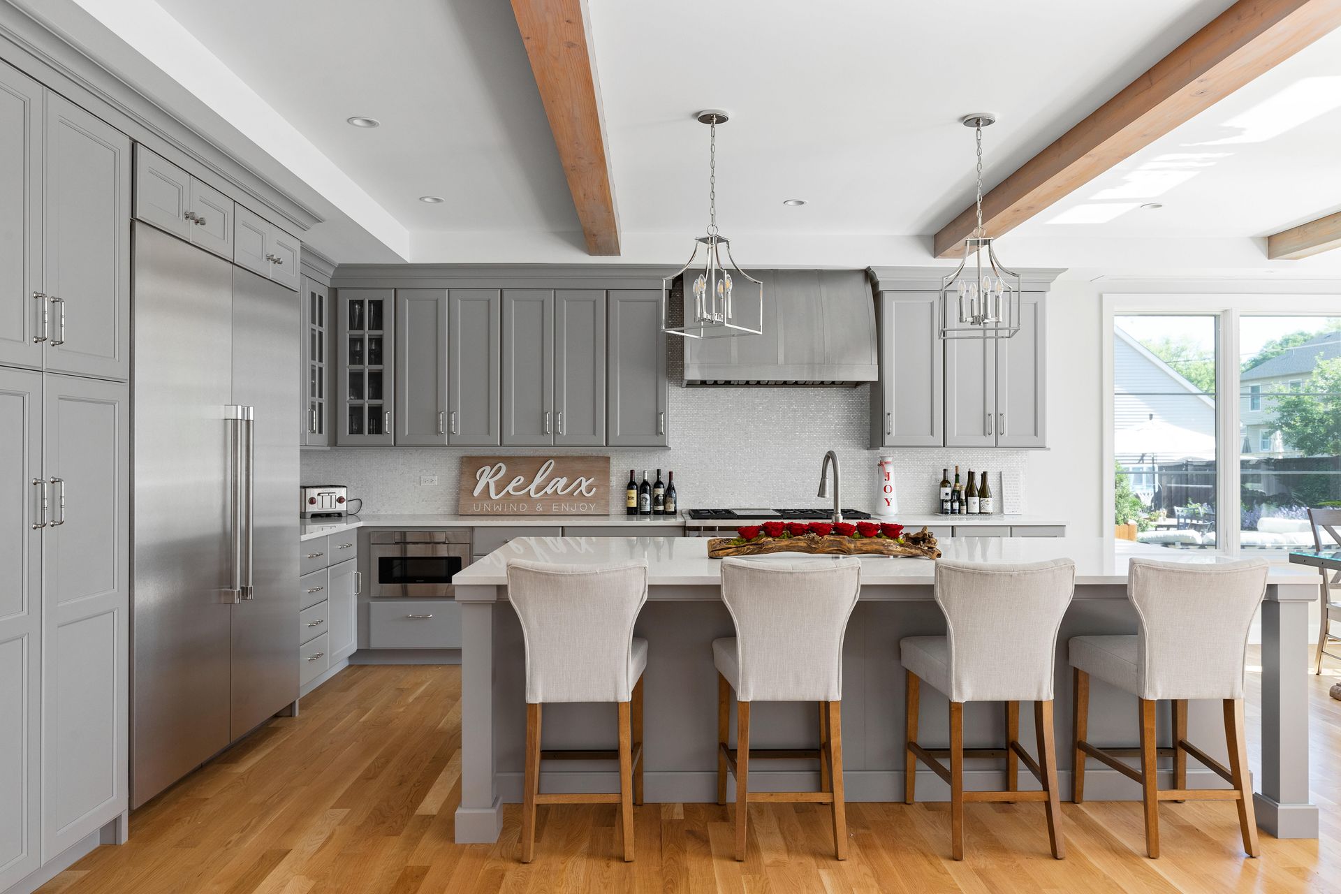 Modern kitchen with gray cabinets, wooden beams, and a white island with bar stools.