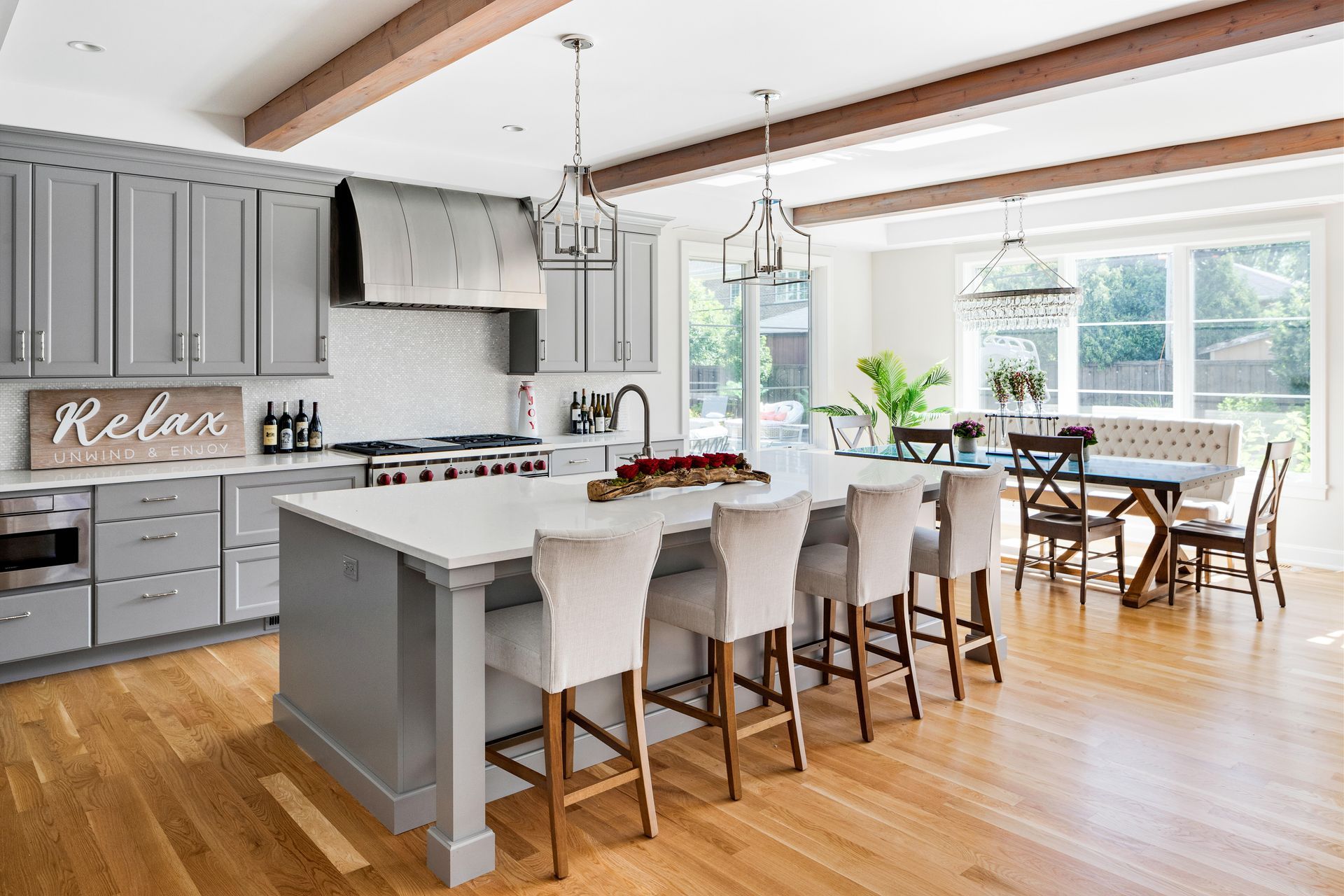 Gray kitchen with white countertops, wooden beams and floors, island with bar stools, and dining area.