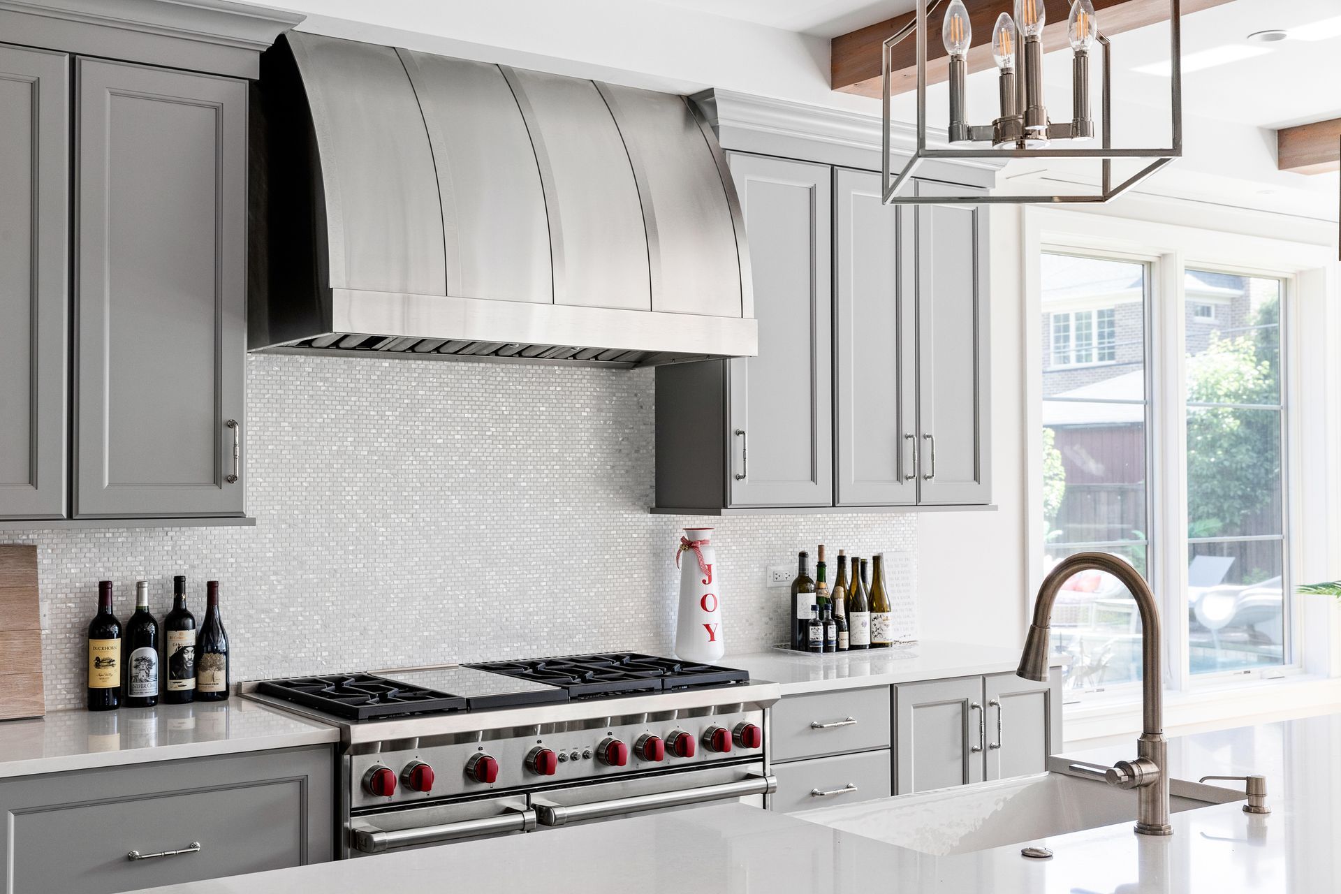 Gray kitchen with stainless steel hood, gray cabinets, white backsplash, and a gas range.