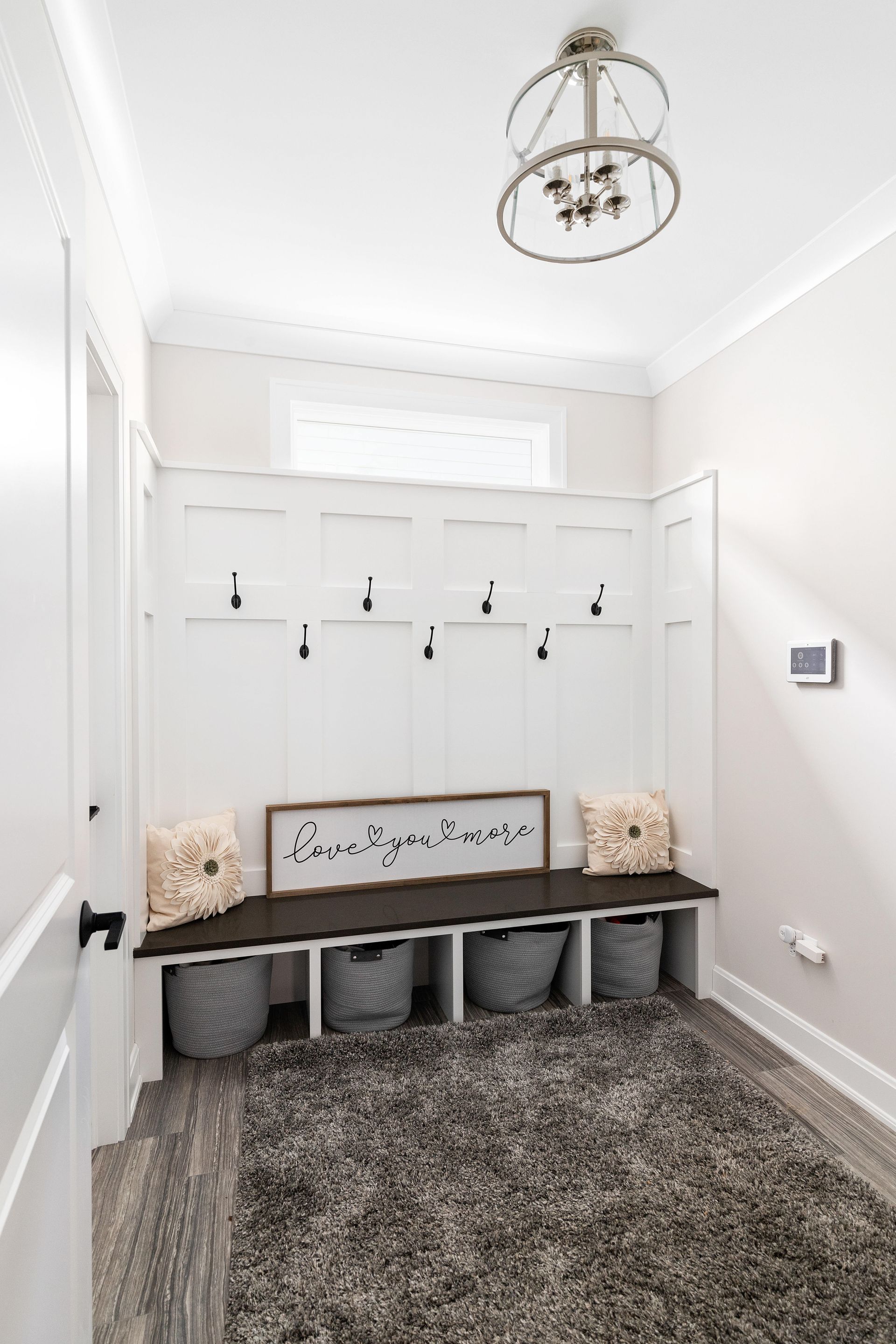 A neutral entryway with a built-in bench, hooks, baskets, rug, and a sign that says 