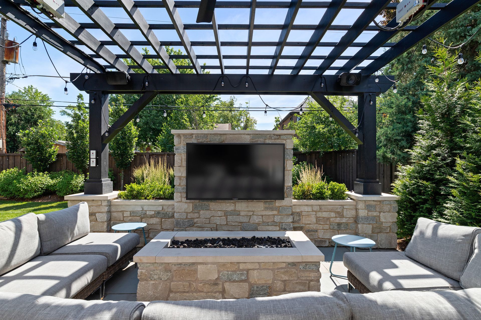 Outdoor living space with stone fireplace, TV, and seating under a pergola.