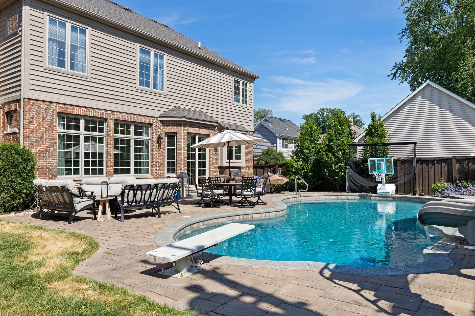 Backyard with pool, patio furniture, and a two-story brick and siding house on a sunny day.