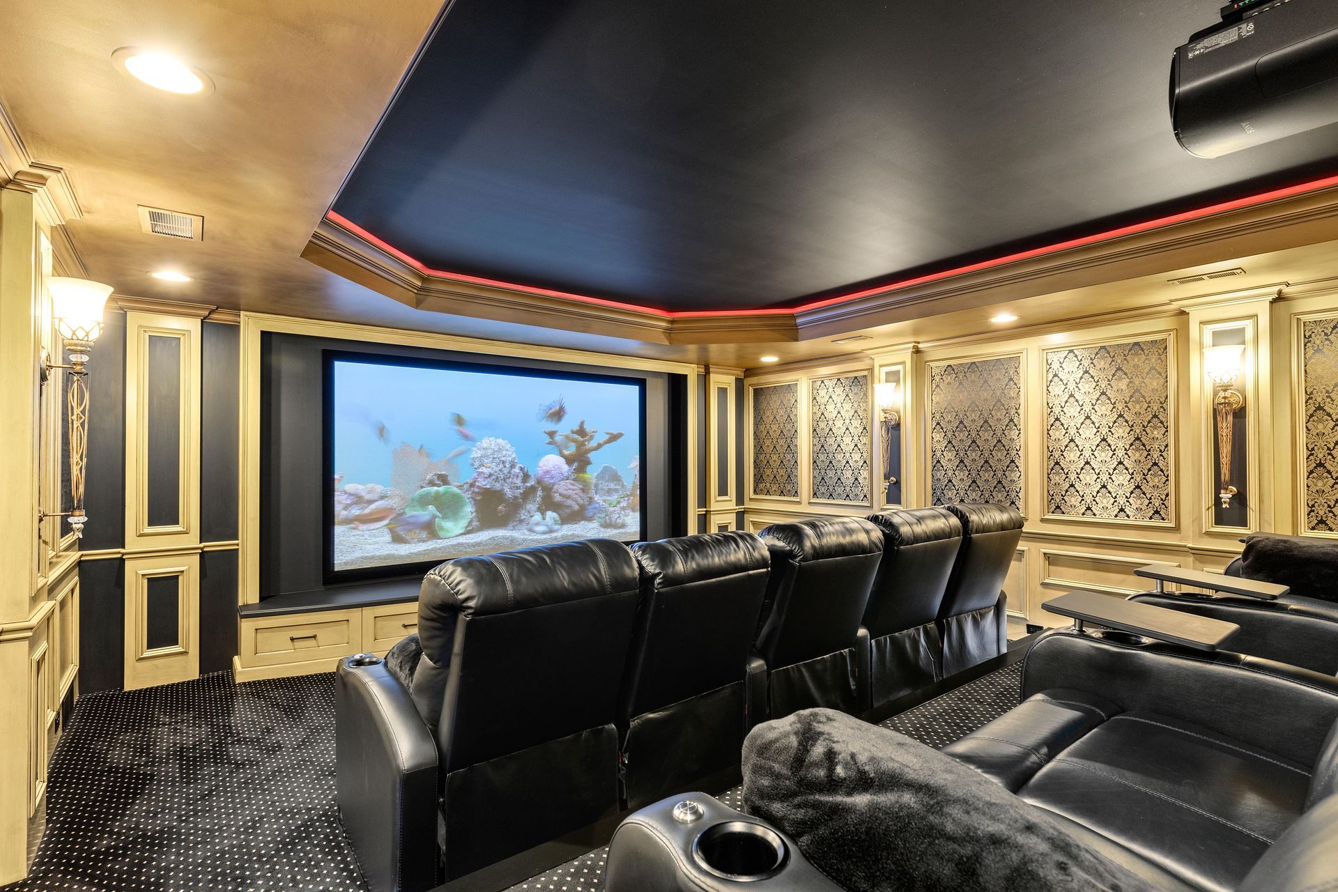 Luxury home theater with black leather recliners, large screen, ornate gold and black trim.