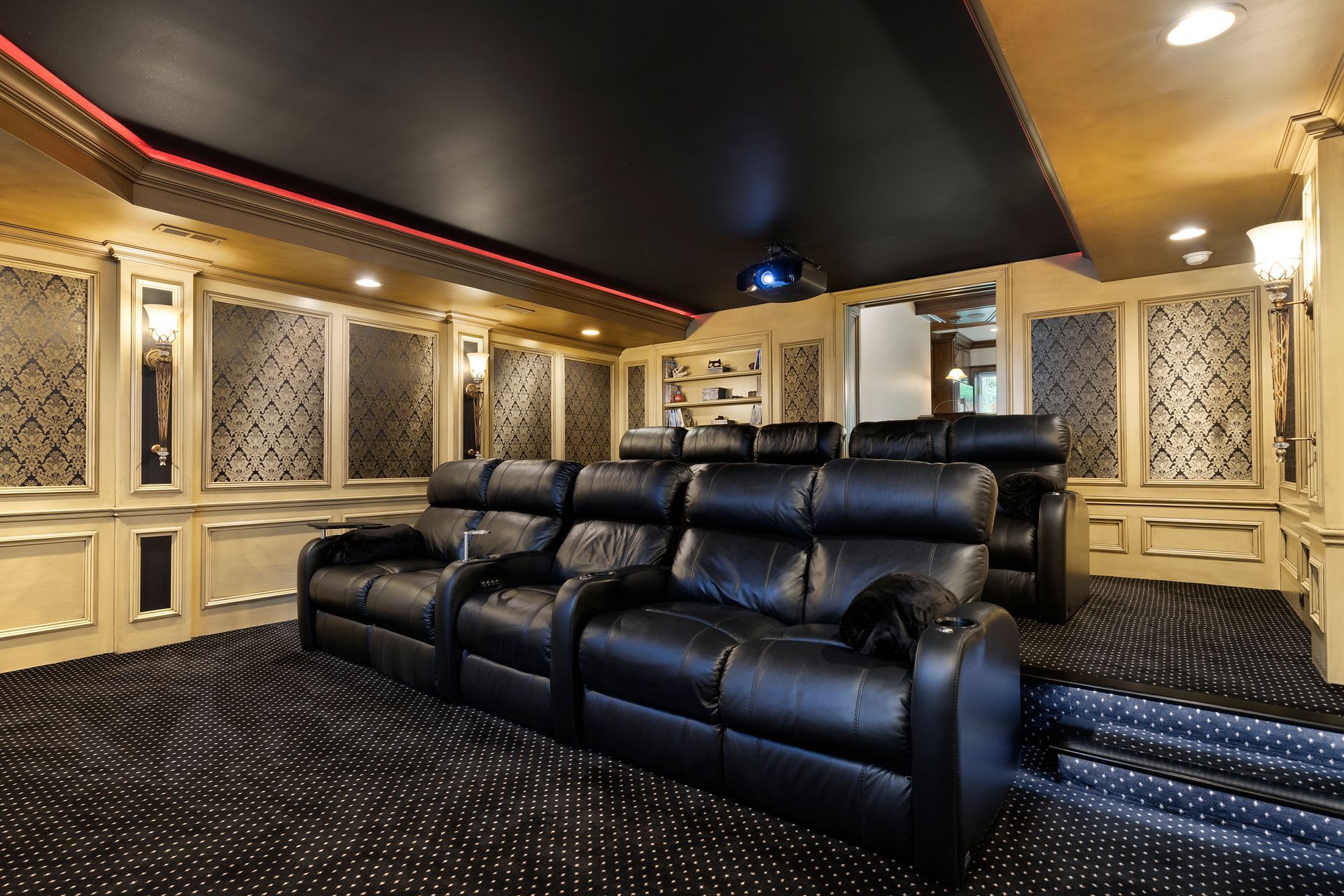 Luxurious home theater with black leather recliners, gold paneling, black ceiling, and projector screen.