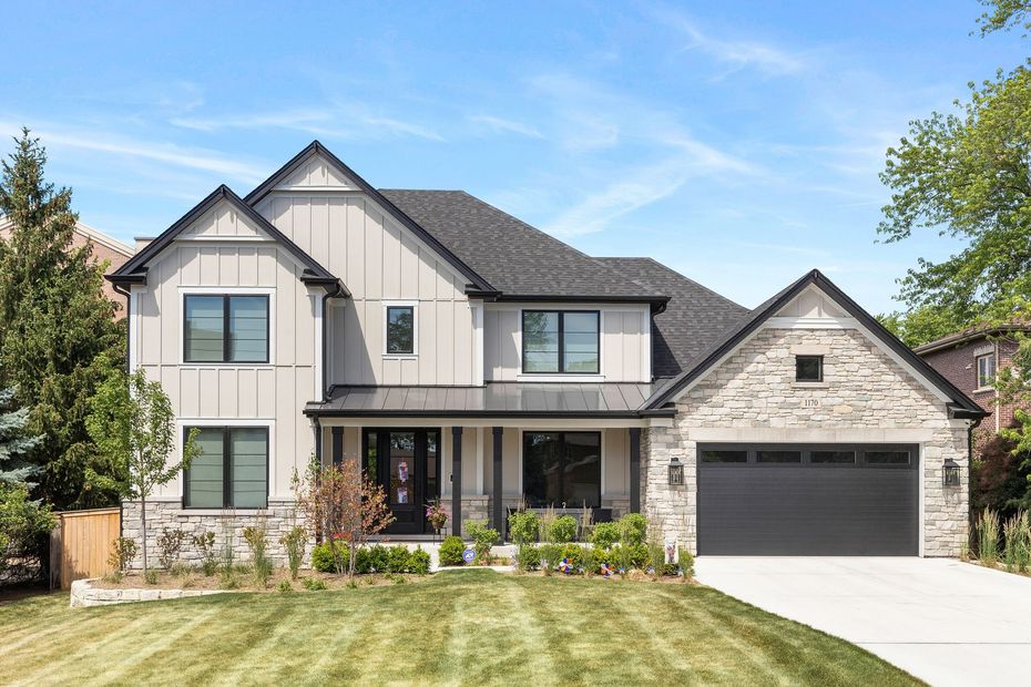 Two-story modern home with gray siding and a stone facade; black roof, windows, and garage door; green lawn.