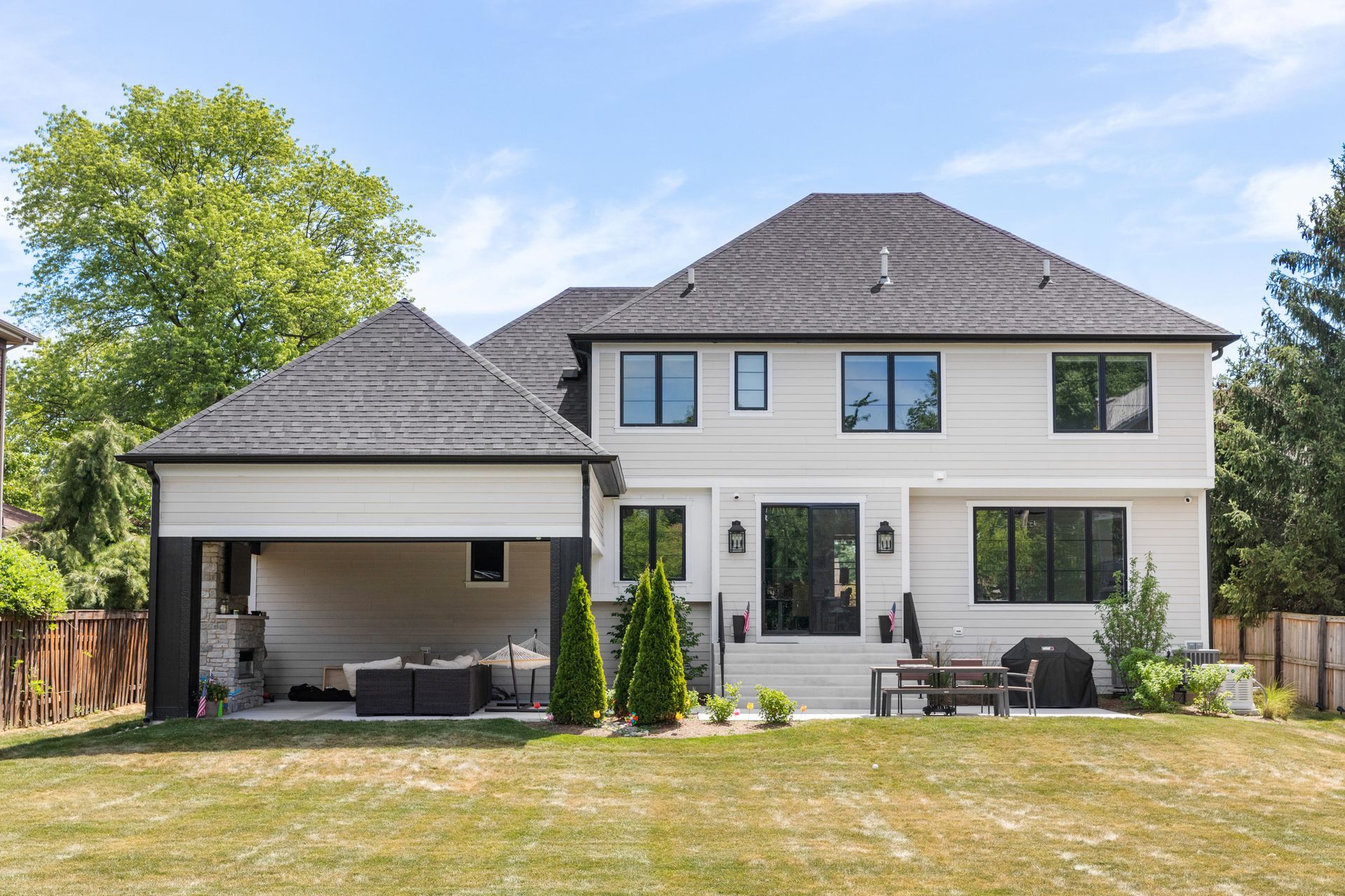 Back exterior of a two-story white house with a covered patio and a grassy backyard on a sunny day.