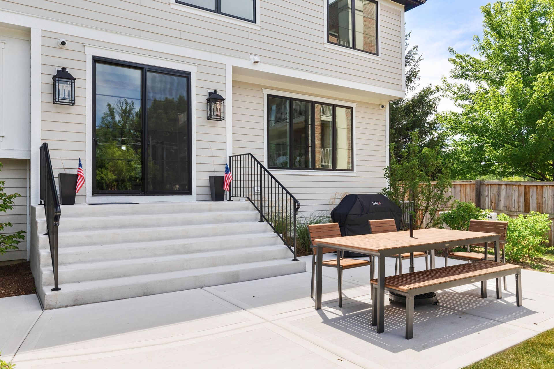 Backyard patio with table, benches, grill, and steps leading to a two-story house.