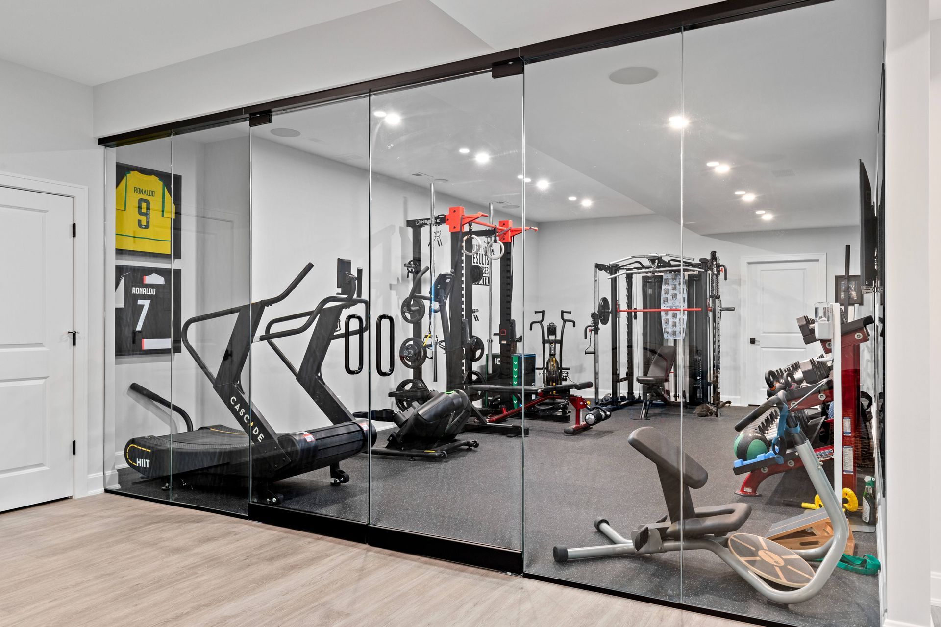 Home gym with glass walls, featuring exercise equipment, including a treadmill and weights.