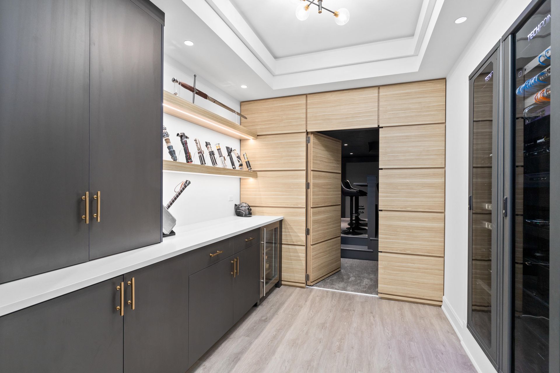 Modern home office with dark grey cabinets, light wood door to gym, wine storage.
