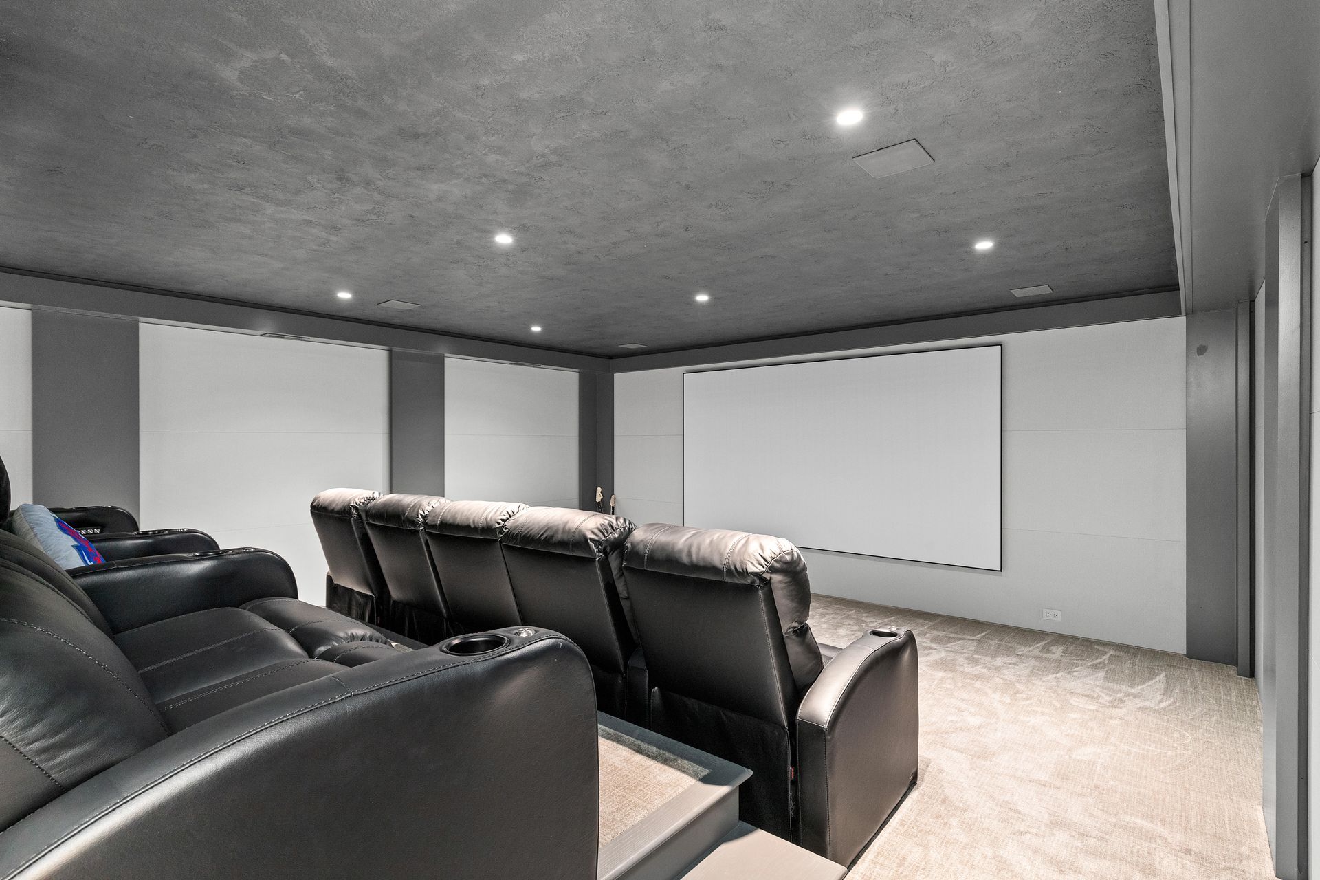 Home theater with black recliners, white screen, gray ceiling, and walls.