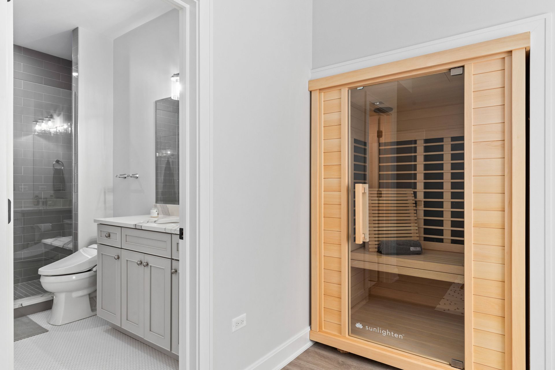 Bathroom with sauna; gray vanity and tile, glass shower, and light wood sauna.