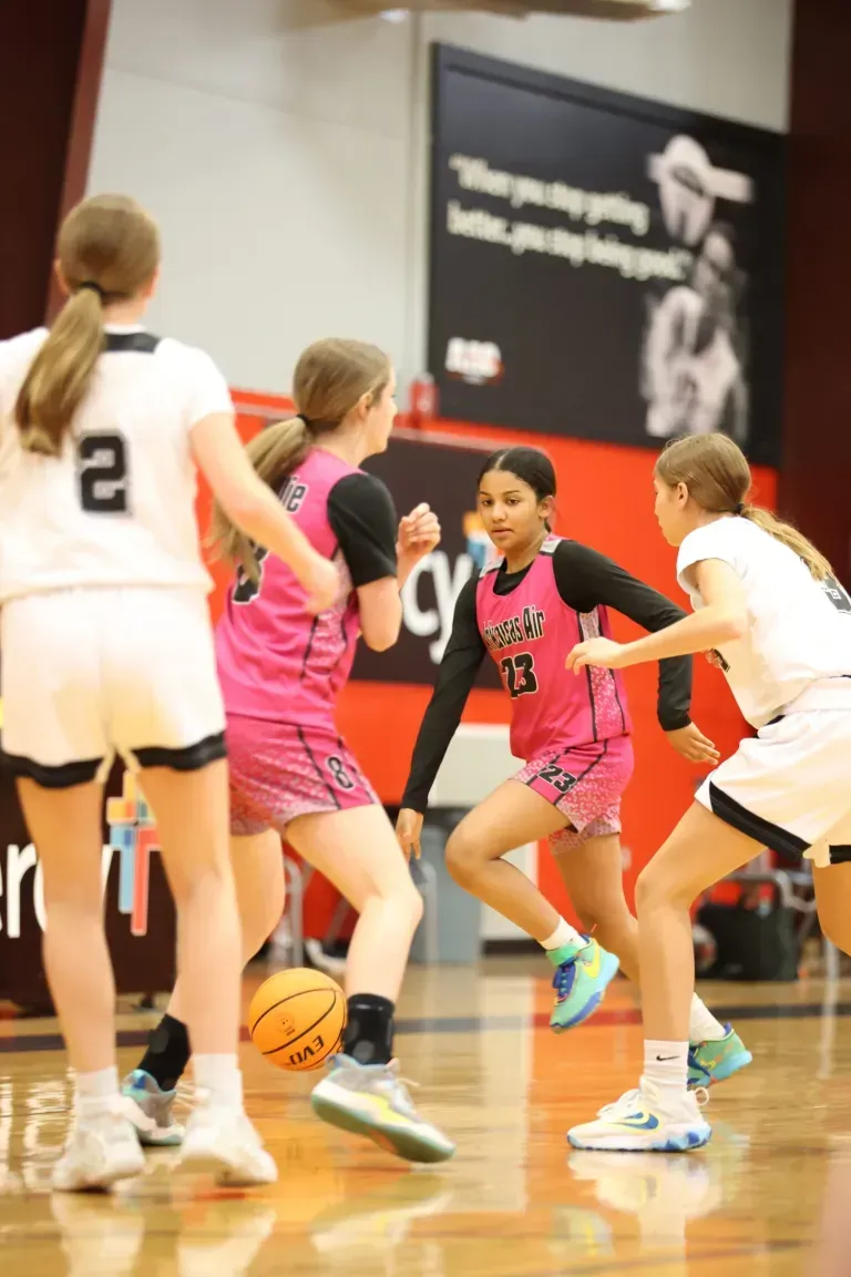 Girl's basketball game in progress; players in pink and white jerseys dribbling the ball.
