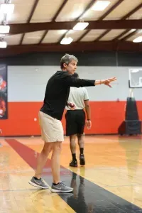 A man in a black shirt and white shorts gesturing on a basketball court.