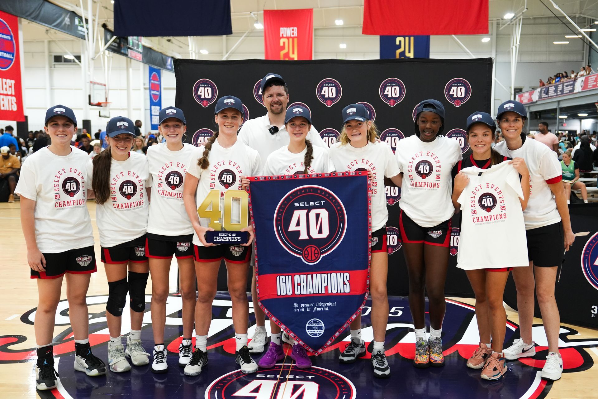 A youth basketball team celebrates their championship win, holding a banner and trophy indoors.