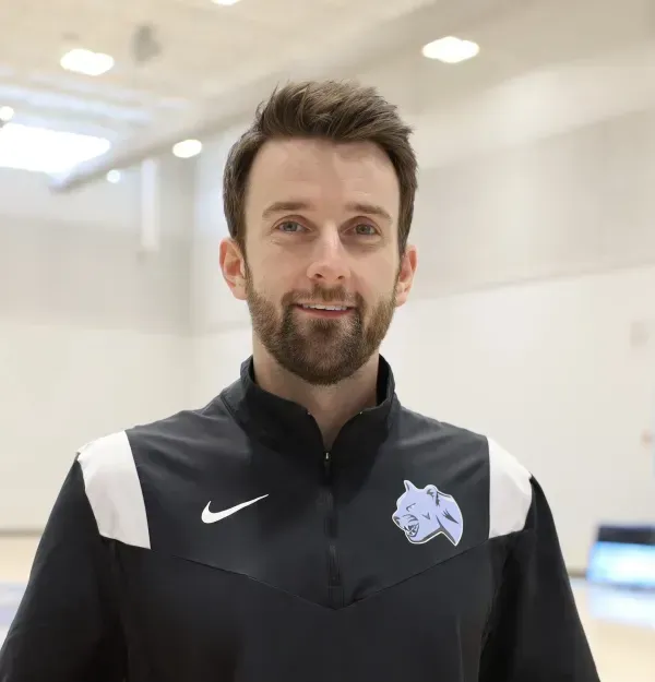 Man smiling, wearing a black athletic jacket with white accents, in a gym setting.